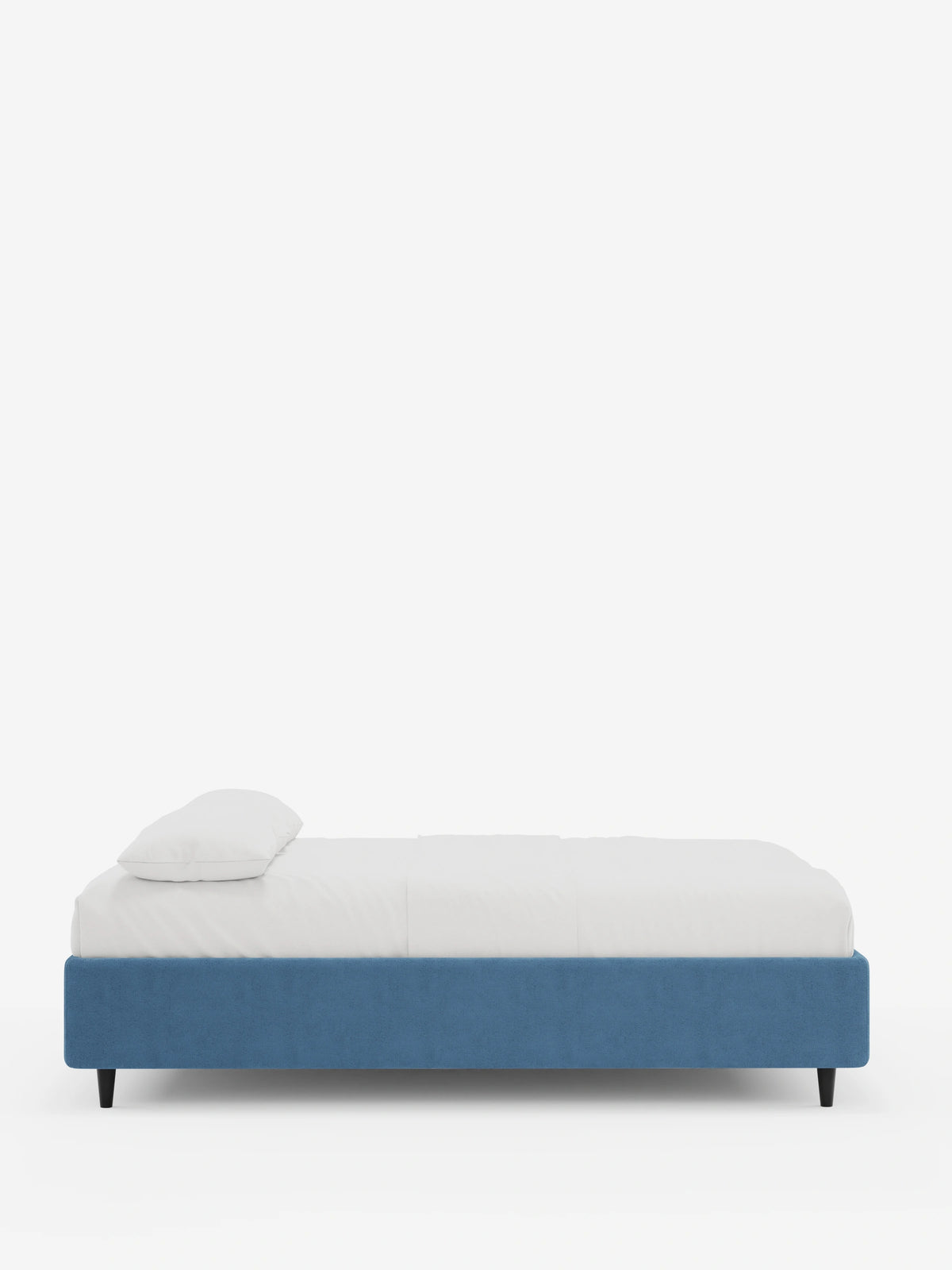 Il letto sommier imbottito ERON con contenitore in tessuto impermeabile certificato Oeko-Tex è un letto moderno, rivestito in blu, caratterizzato da una base dalle linee pulite, un unico cuscino bianco e gambe corte, scure e cilindriche che risaltano sullo sfondo bianco.
