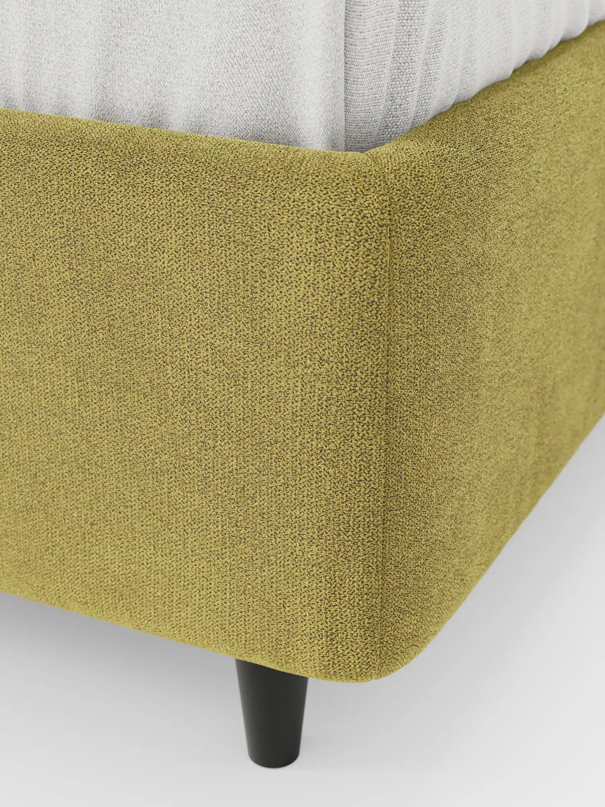Primo piano di un letto sommier imbottito ERON con vano contenitore in tessuto impermeabile certificato Oeko-Tex, che mostra il tessuto verde chartreuse a trama in rilievo su una gamba cilindrica scura affusolata, con un materasso bianco visibile nella parte superiore.
