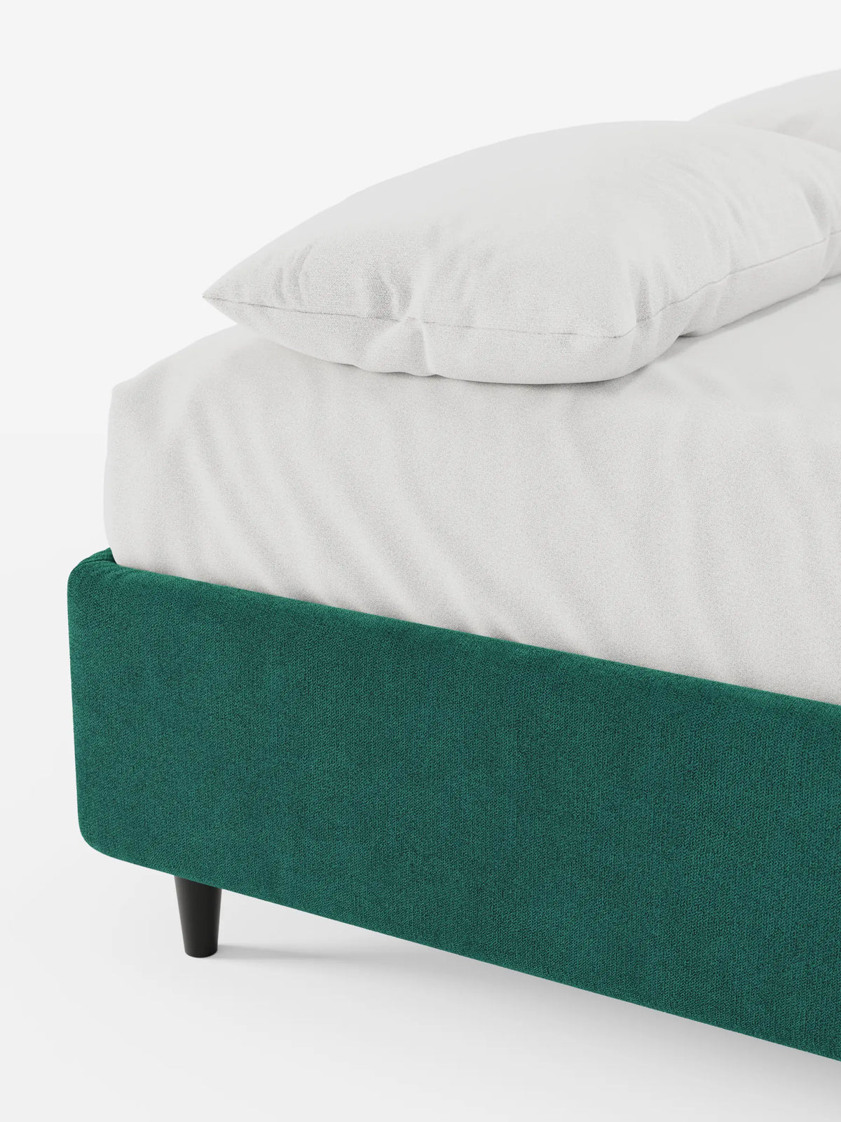 Un primo piano di un letto sommier ERON verde smeraldo, imbottito e dotato di vano contenitore in tessuto impermeabile certificato Oeko-Tex, rivestito con biancheria da letto bianca e due cuscini, su uno sfondo chiaro a tinta unita.