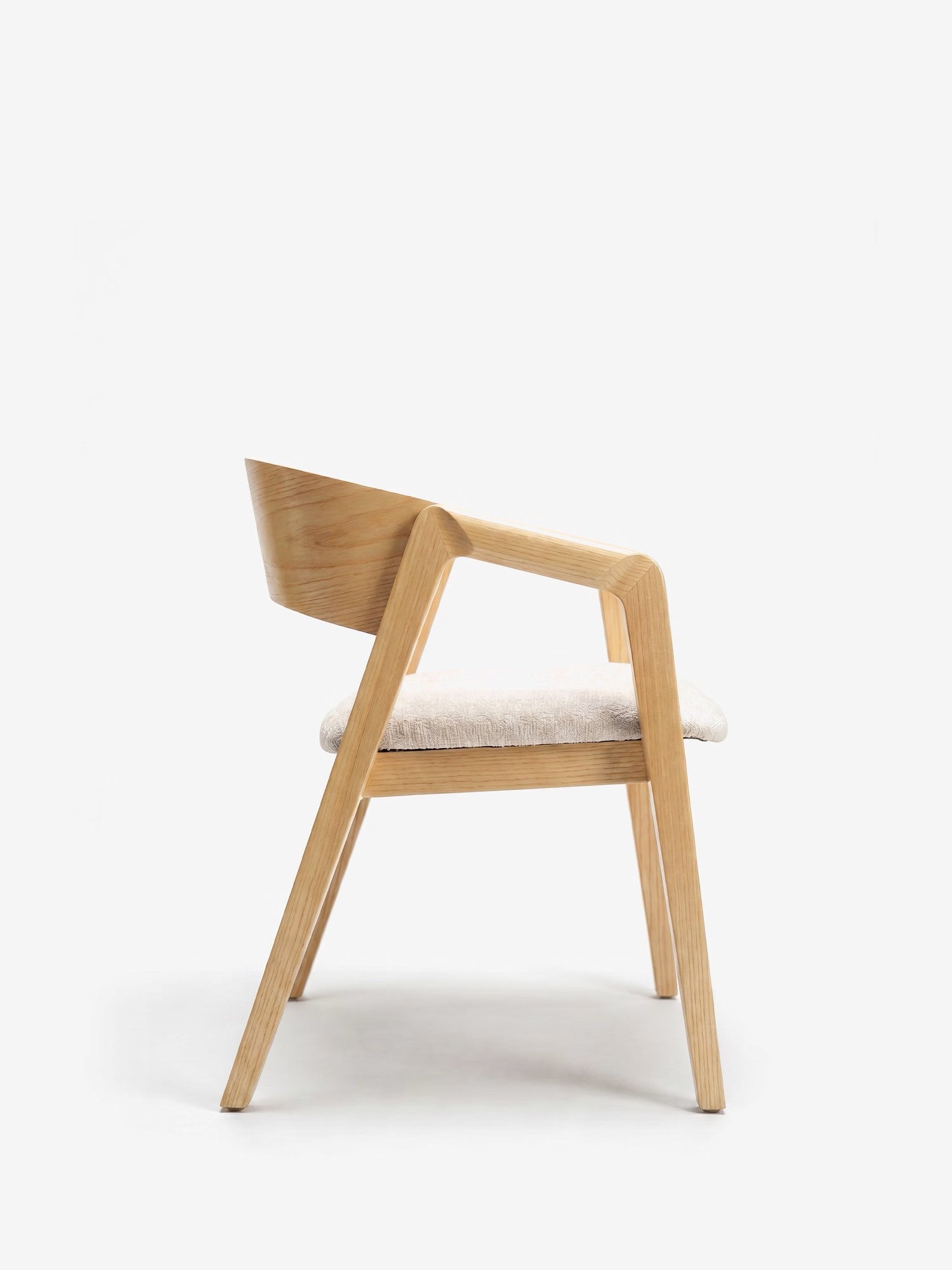 La sedia Etra in legno massello naturale di Divani.Store presenta braccioli e tessuto OEKO-TEX®, un design moderno e naturale con gambe inclinate, schienale curvo e seduta imbottita color beige chiaro, raffigurata di profilo su sfondo bianco.