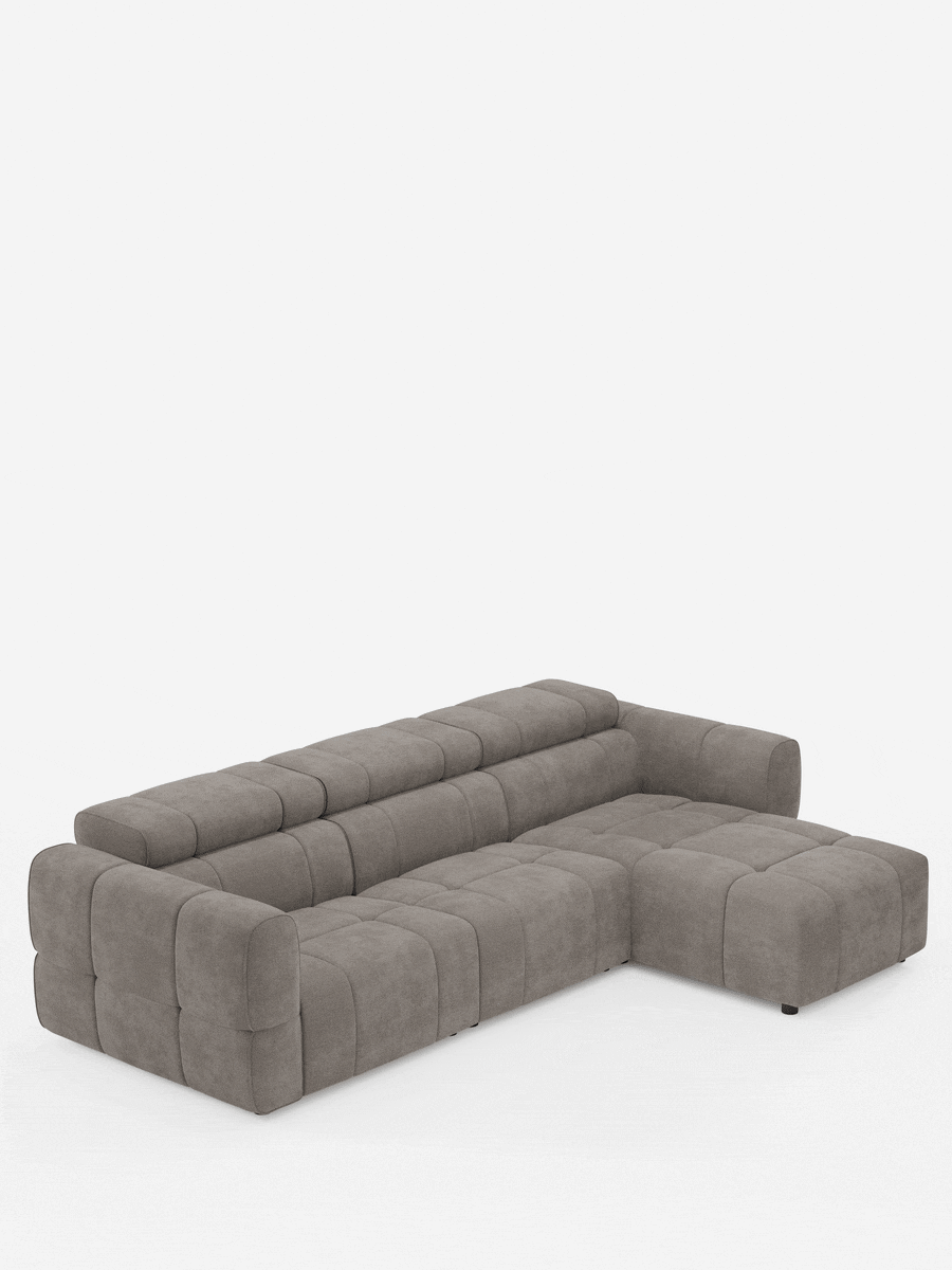 Un divano angolare modulare Giotto grigio a 5 posti da 296 cm con penisola e funzione relax elettrica opzionale, rivestito in tessuto antimacchia T23, caratterizzato da un profilo basso e da un motivo trapuntato a griglia su sfondo bianco.