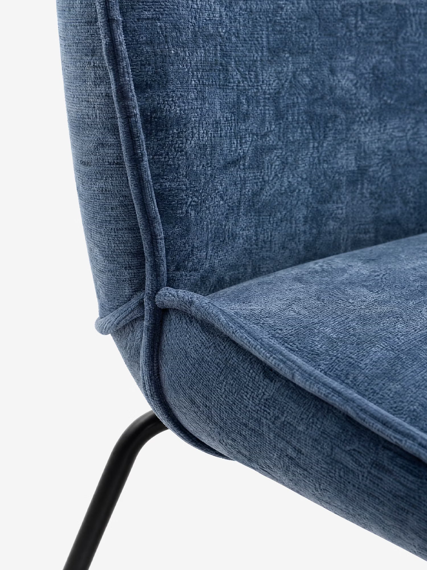 Primo piano della sedia imbottita Iride di Divani.Store, caratterizzata da un morbido tessuto materico blu intenso, cuciture rifinite, seduta e schienale curvi e una gamba in metallo nero a vista: eleganza moderna per qualsiasi ambiente.
