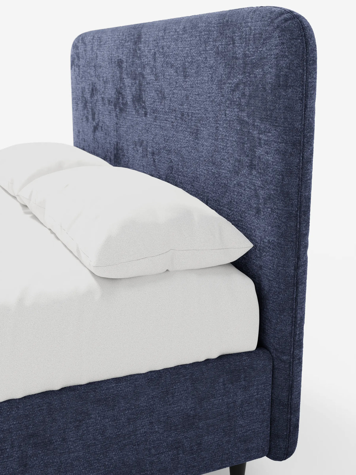 Un primo piano del letto imbottito KAELOS Letto Minimal, caratterizzato da una testiera arrotondata blu scuro in morbido tessuto ciniglia testurizzato, rivestito con un lenzuolo bianco e due cuscini su uno sfondo bianco e pulito.