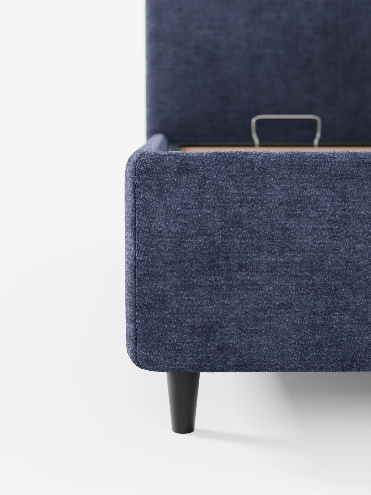 Un primo piano di un divano KAELOS Letto Minimal imbottito blu scuro - con vano contenitore, piedini alti e testiera arrotondata in tessuto ciniglia con finitura testurizzata e gambe affusolate, raffigurato parzialmente aperto per mostrare lo spazio contenitivo e una maniglia in metallo.