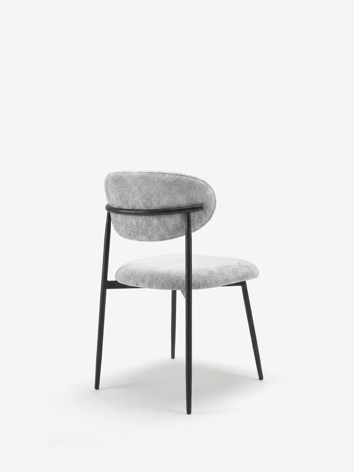 La Luce Sedia, imbottita in morbida ciniglia di Divani.Store, presenta una seduta soffice di colore grigio chiaro, uno schienale arrotondato e un'elegante struttura in metallo nero con sottili gambe inclinate, raffigurata di profilo su uno sfondo bianco.