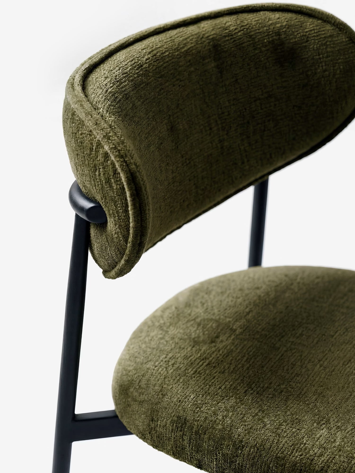 Un primo piano della Luce Sedia, imbottita in morbido tessuto ciniglia di Divani.Store, caratterizzata da seduta e schienale curvi in tessuto testurizzato verde oliva, montati su un'elegante struttura in metallo nero su sfondo bianco, per un look moderno.