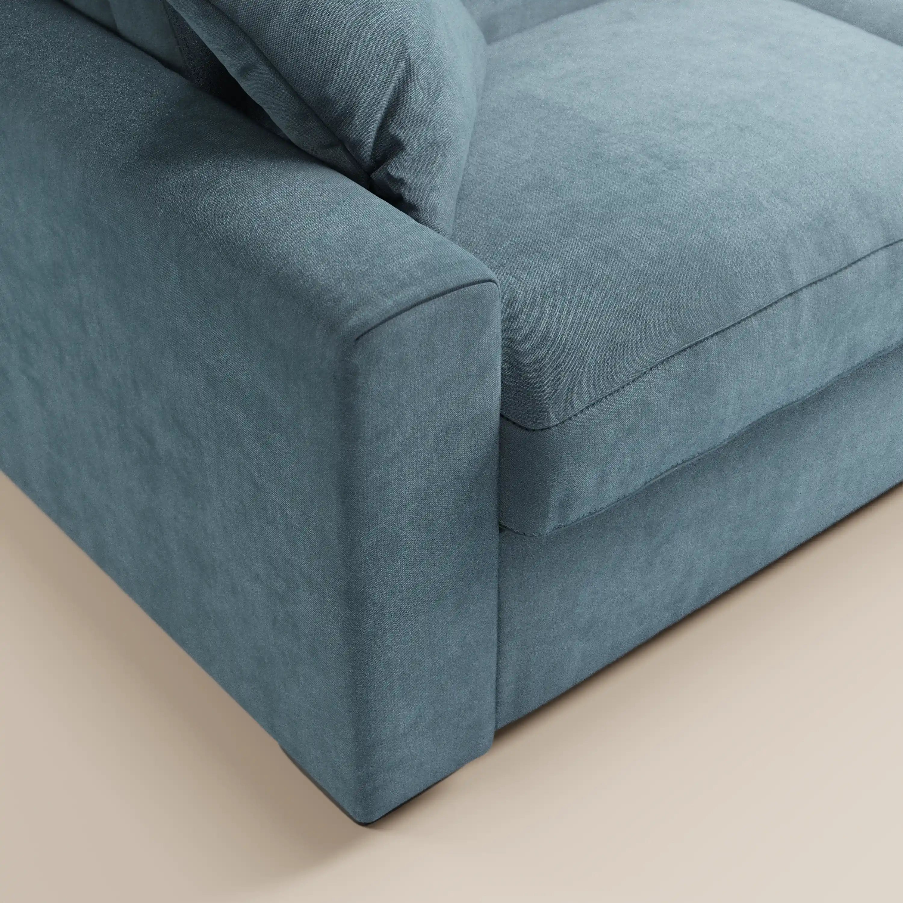 Primo piano del divano letto a 3 posti Maximus di Divani.Store, realizzato in tessuto blu Oeko-Tex antimacchia, caratterizzato da braccioli spessi, seduta imbottita, poggiatesta reclinabile e materasso alto 20 cm. Il comfort moderno risalta sul pavimento chiaro.
