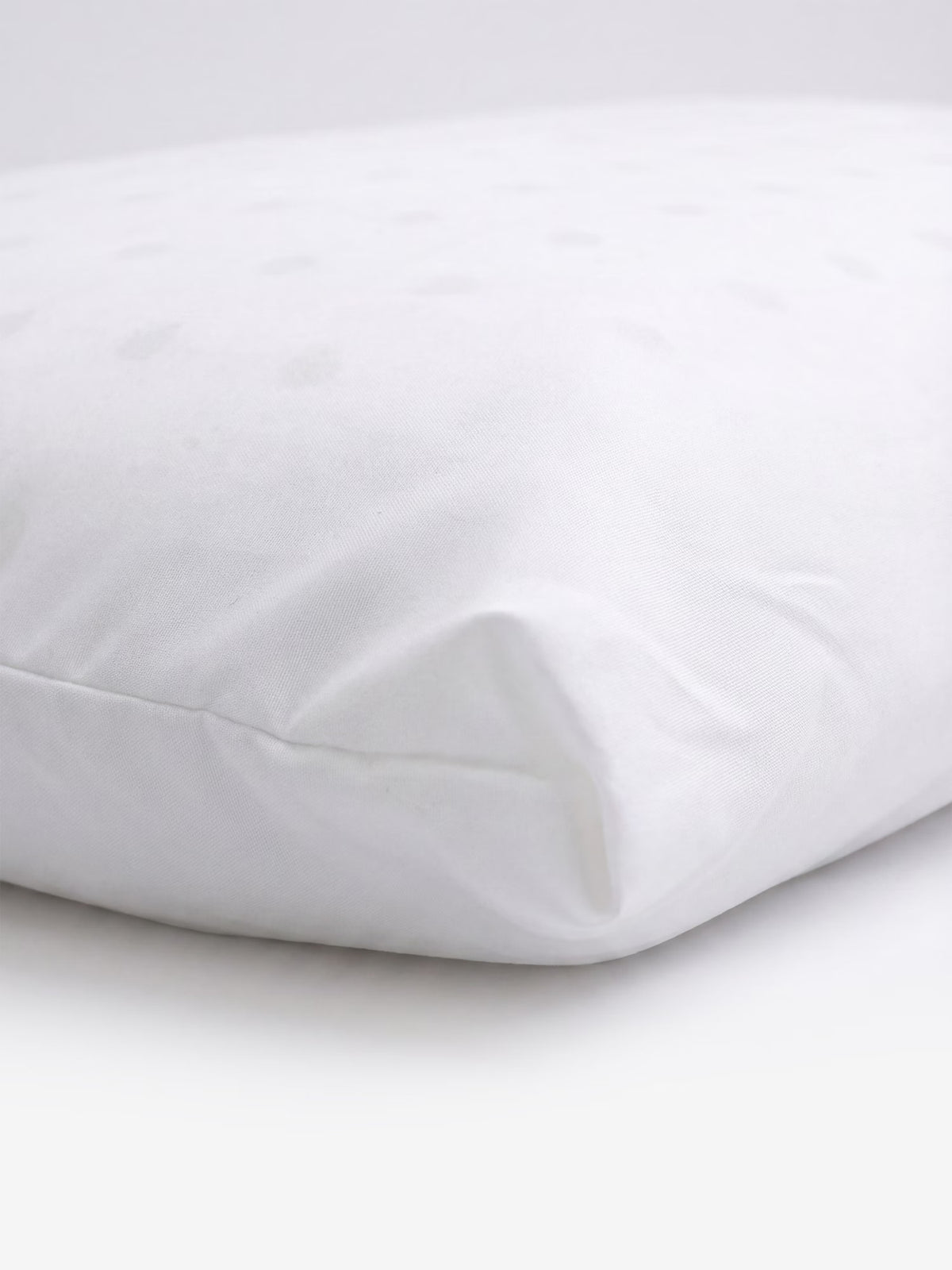 Un primo piano dell'angolo del guanciale KYROS-PRIME in memory foam a iniezione, personalizzato e ortopedico di Divani.Store mette in risalto il suo rivestimento in tessuto bianco e liscio, caratterizzato da una texture delicata. Il cuscino è posizionato su uno sfondo bianco e appare pulito e soffice, a sottolineare il comfort e il sostegno cervicale. I motivi a pois appena visibili sulla superficie superiore ne esaltano il fascino come cuscino ortopedico progettato per un allineamento ottimale del collo.