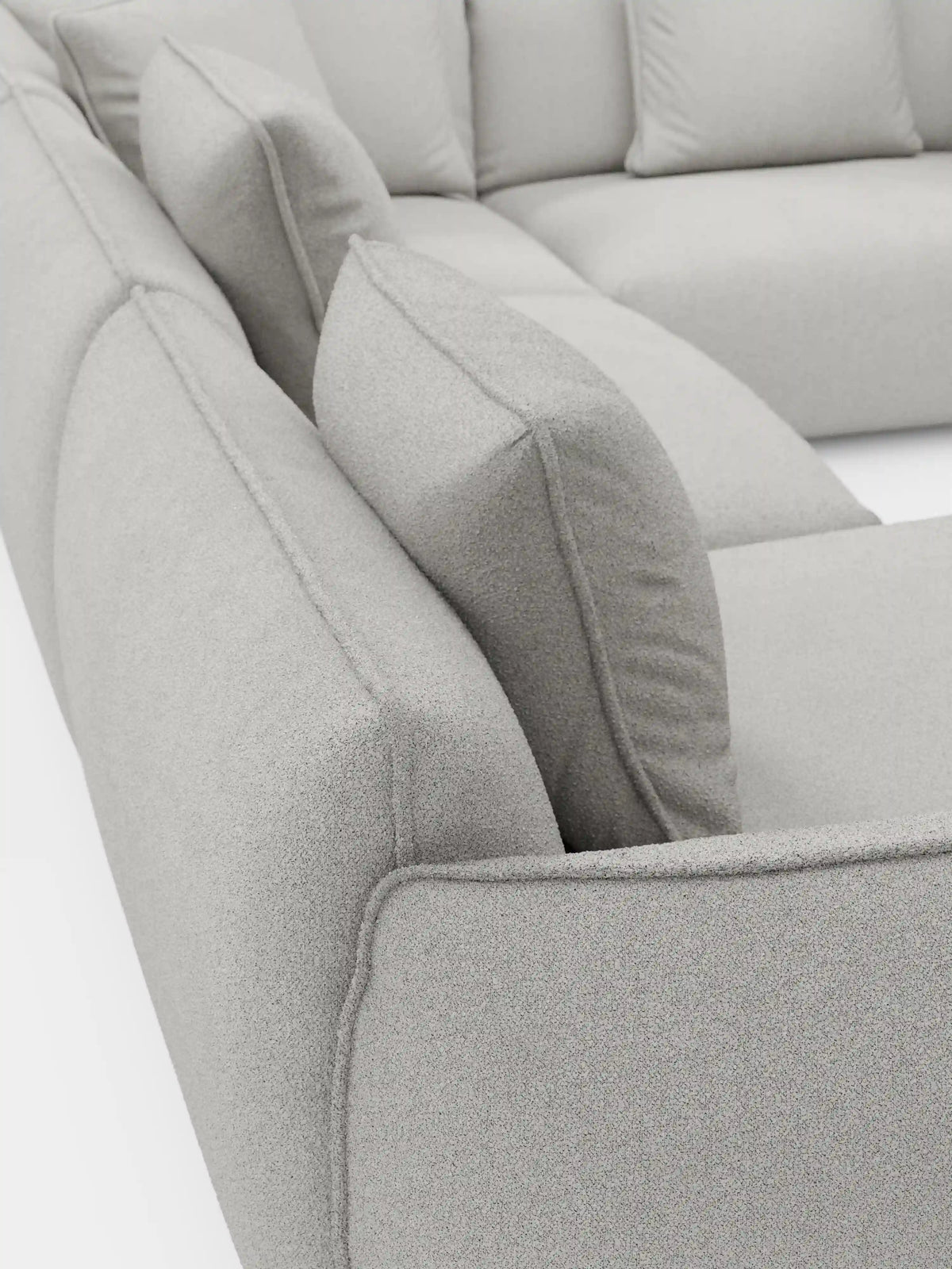 Primo piano del divano angolare panoramico componibile Nimbus con penisola e angolo in tessuto smacchiabile T33 di Divani.Store, caratterizzato da un divano modulare italiano di colore grigio chiaro. I morbidi cuscini quadrati e il tessuto soffice, strutturato e antimacchia mettono in risalto l’imbottitura spessa e le cuciture pulite e moderne. Le sezioni angolari della seduta e dello schienale esaltano sia il comfort che il design contemporaneo.