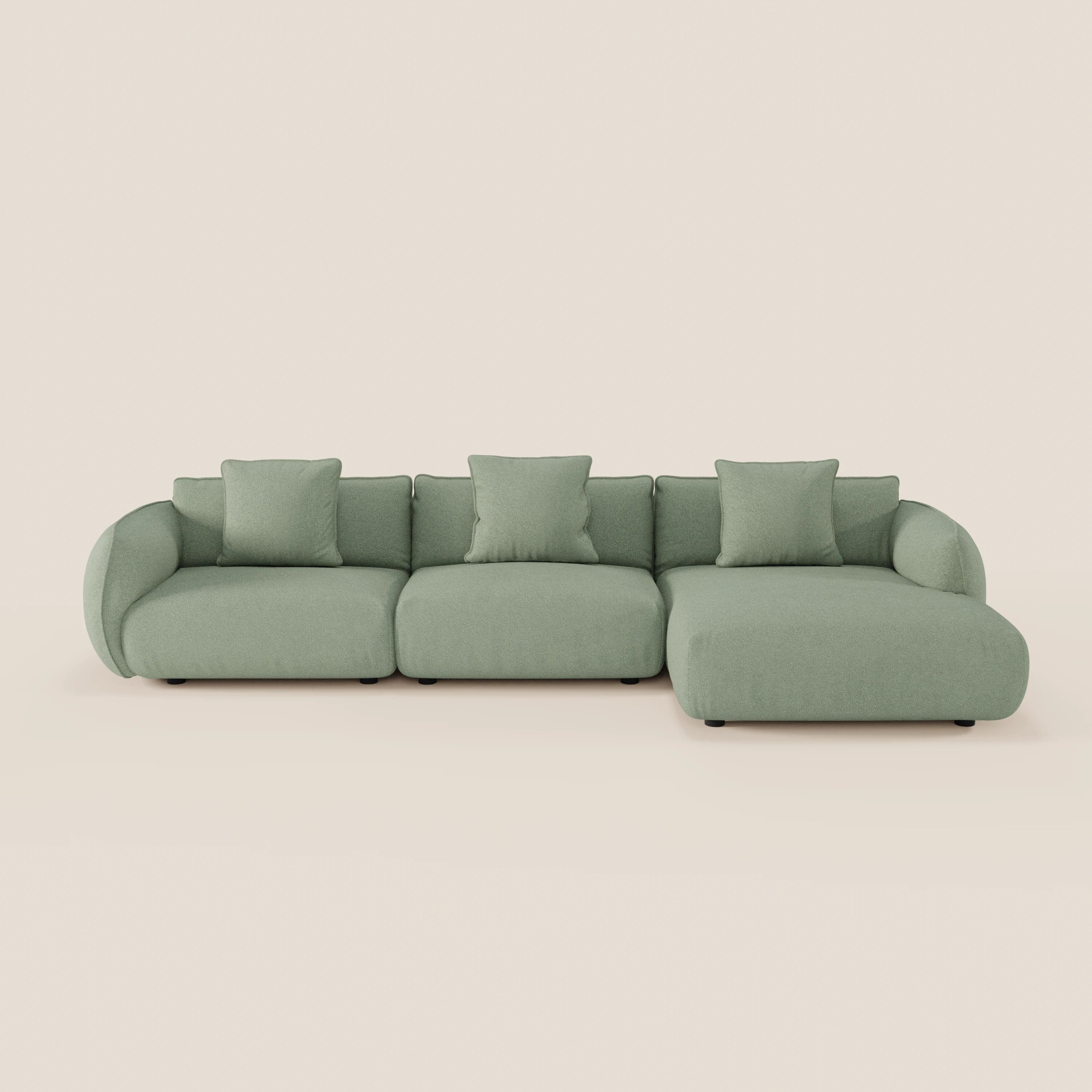 Il divano Nimbus angolare con penisola componibile di Divani.Store è un moderno divano verde chiaro in morbido tessuto effetto cotone antimacchia con tre posti, chaise lounge destra, braccioli e schienali arrotondati e quattro cuscini coordinati su sfondo beige.