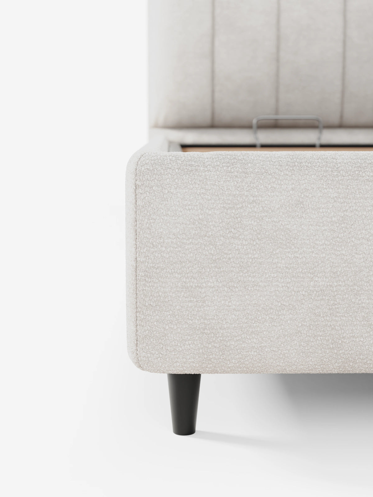 Primo piano di un letto imbottito ONYX con contenitore e testiera verticale in tessuto certificato Oeko-Tex® color beige chiaro con finitura testurizzata, caratterizzato da una testiera rettangolare con cuciture verticali e da una gamba affusolata nera.