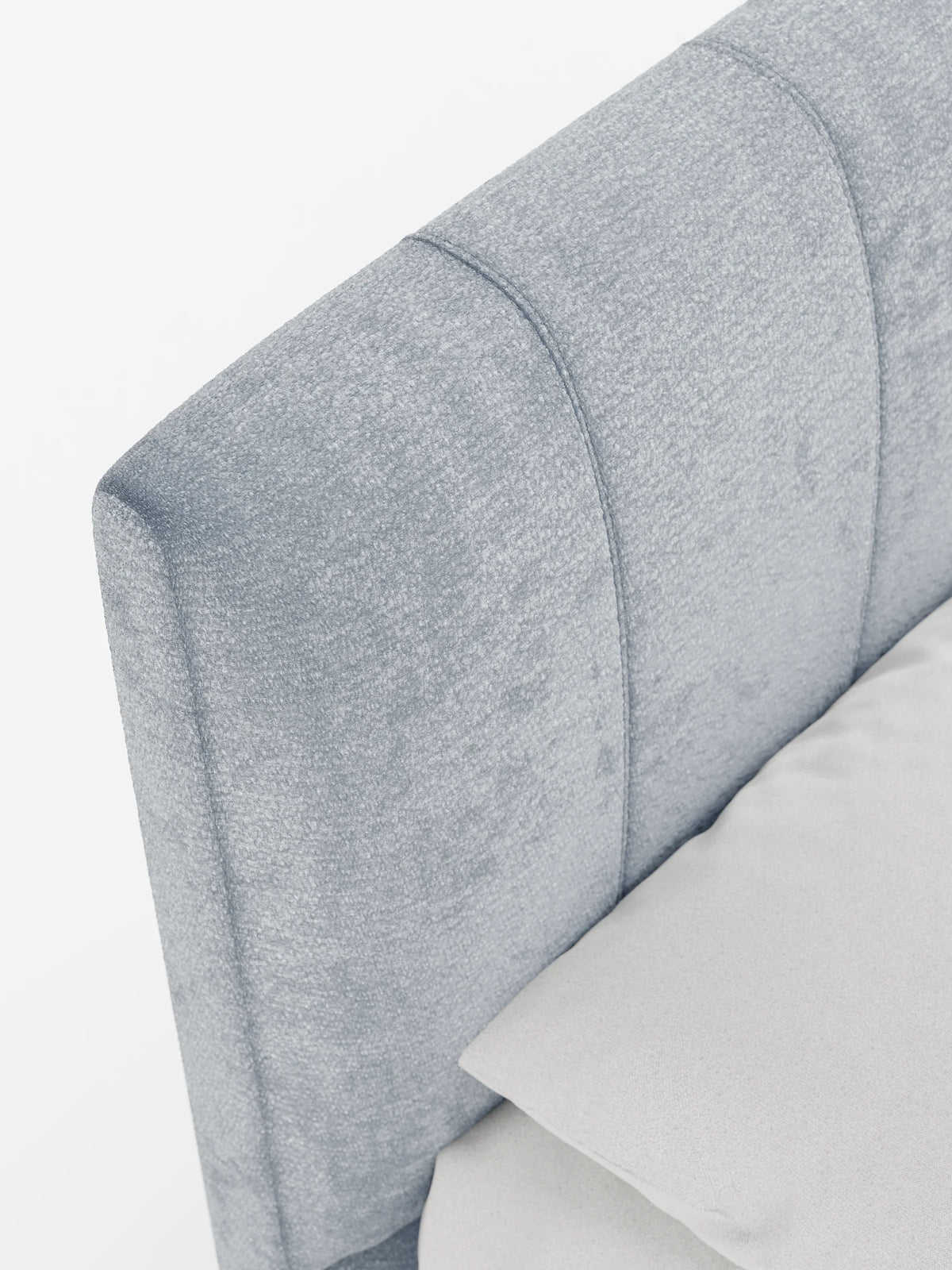 Un primo piano in angolazione della testiera imbottita, di colore grigio chiaro e dalla trama ruvida, di un letto ONYX imbottito con contenitore e testiera verticale in tessuto certificato Oeko-Tex®, caratterizzata da pannelli verticali accanto a un cuscino liscio abbinato.