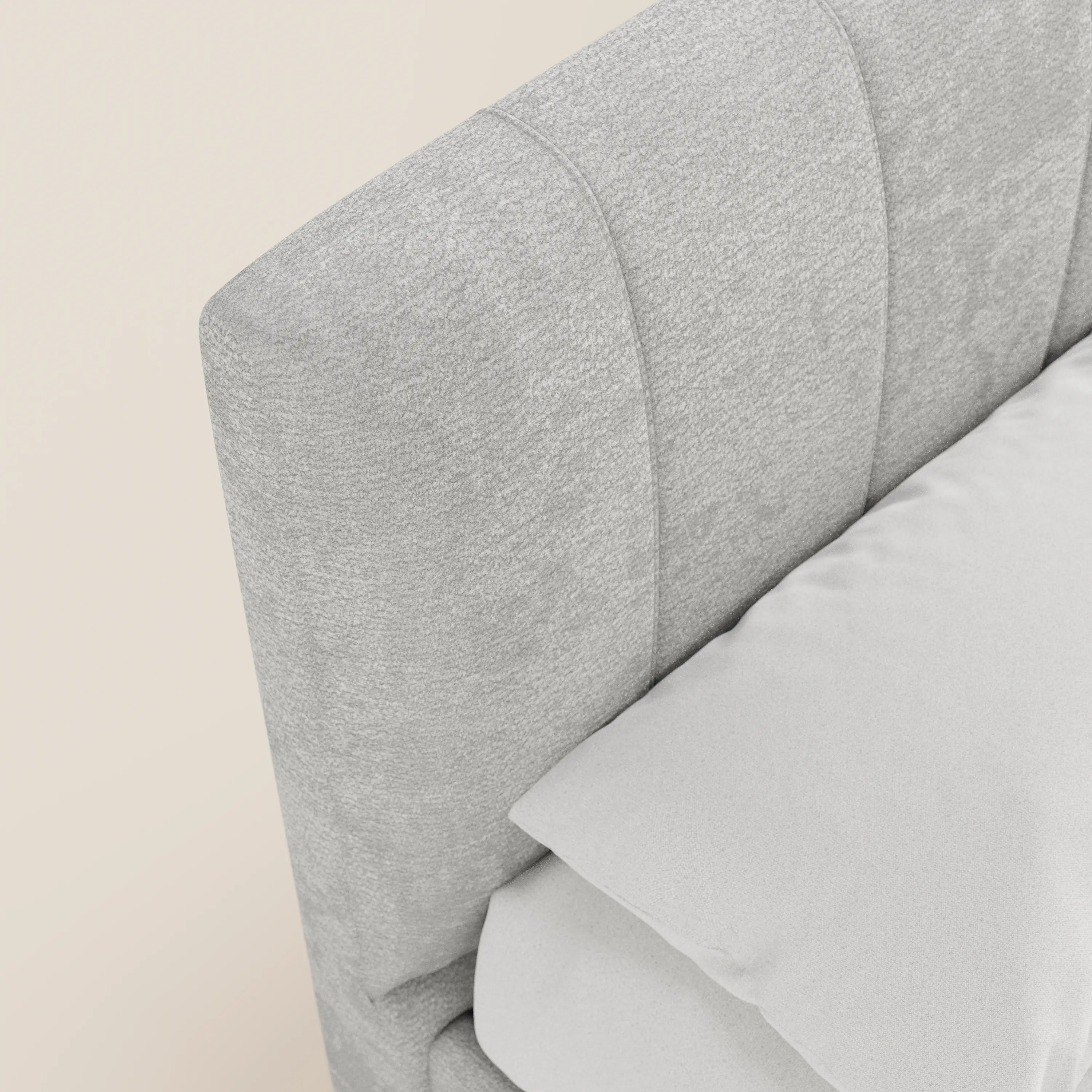 Primo piano del letto imbottito ONYX con contenitore di Letti.store, con testiera verticale in tessuto Oeko-Tex®, grigio chiaro e tre cuciture verticali. Il letto appare ordinato, con un cuscino e un lenzuolo bianco su uno sfondo color avorio.