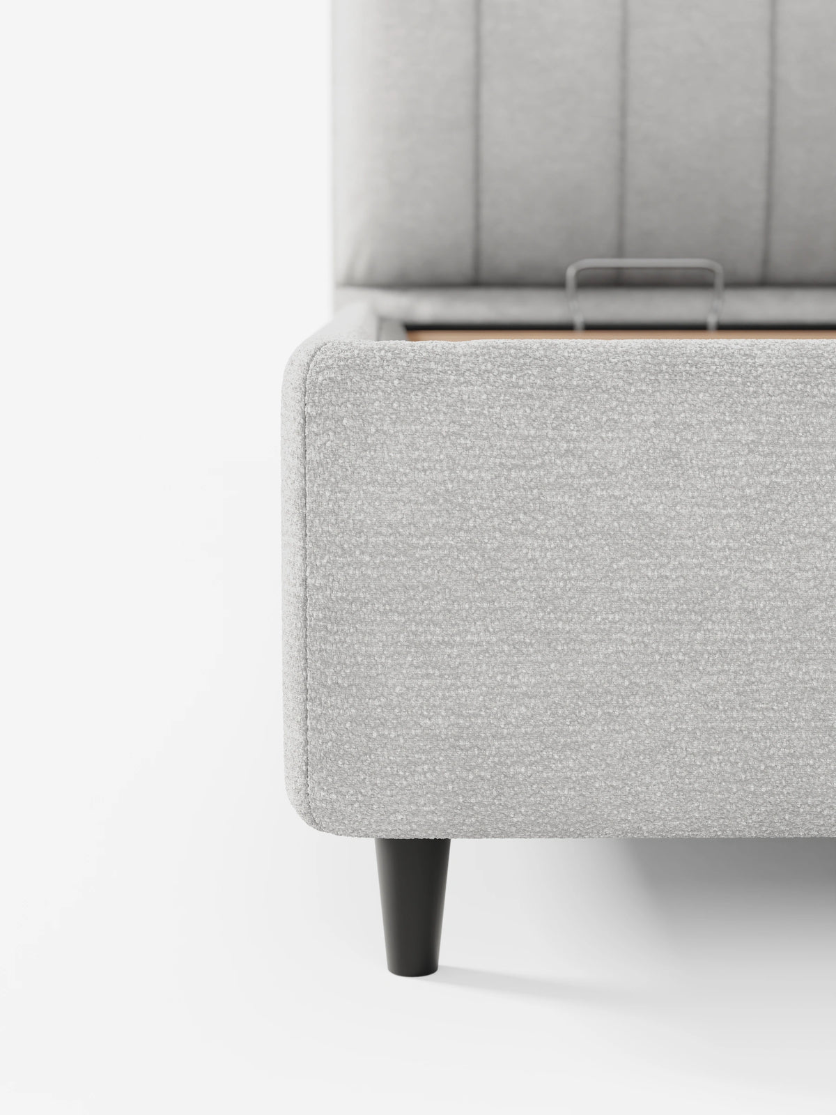 Un primo piano del letto imbottito ONYX con vano contenitore e testiera verticale in tessuto certificato Oeko-Tex® color grigio chiaro, caratterizzato da una testiera con trapuntatura verticale, gambe affusolate scure e una base rialzata che rivela un vano contenitore.
