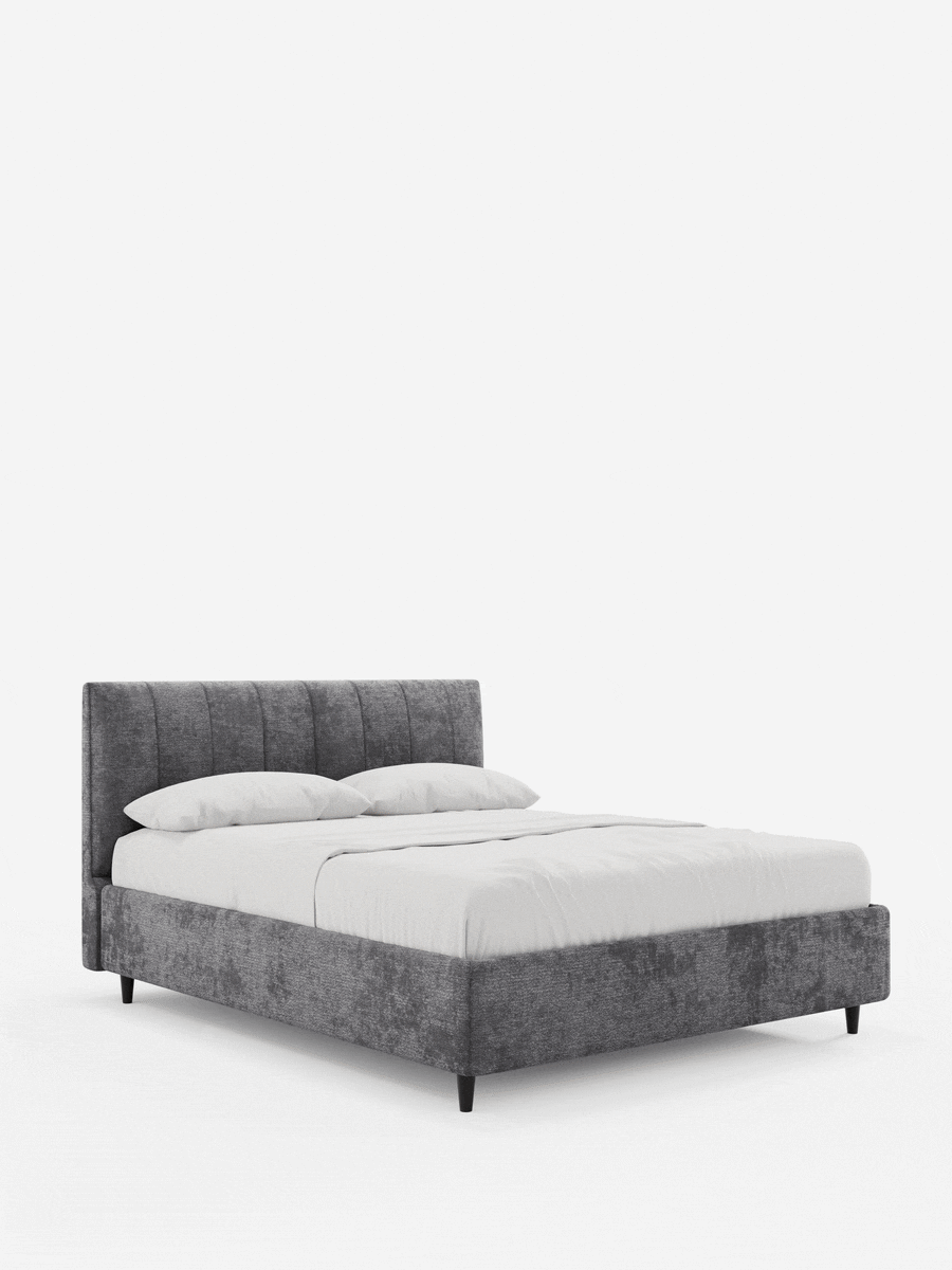 ONYX, letto imbottito con contenitore e testiera verticale in tessuto certificato Oeko-Tex®, caratterizzato da un'alta testiera a pannelli verticali di colore grigio scuro, rivestita con lenzuola bianche, su gambe corte e affusolate di colore nero, su uno sfondo bianco a tinta unita.