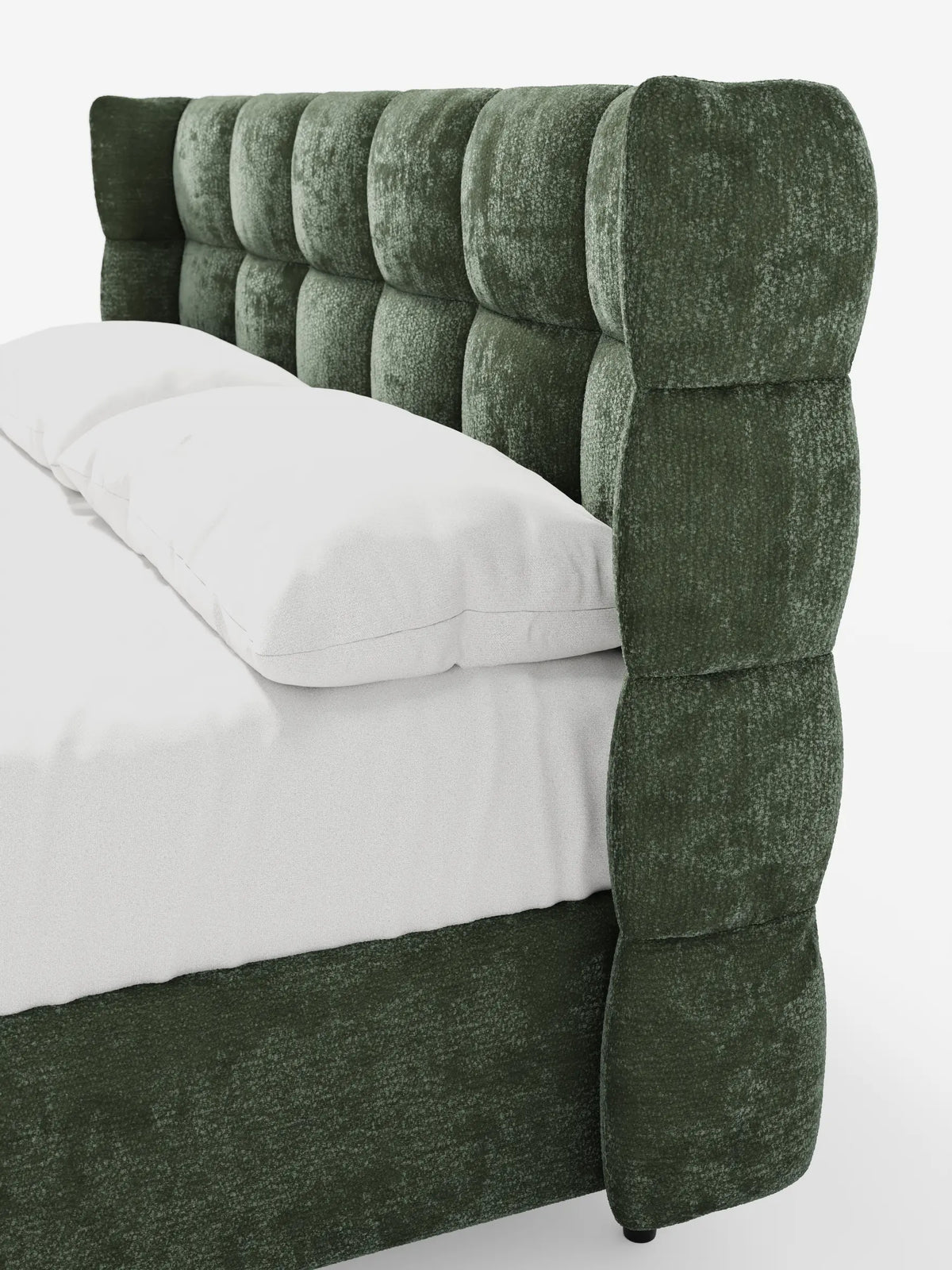 Un letto imbottito RAGNAR color verde bosco, con contenitore e testiera capitonné avvolgente, caratterizzato da un’alta testiera capitonné avvolgente, rivestito con lenzuola bianche immacolate e due cuscini bianchi su uno sfondo chiaro e sobrio.