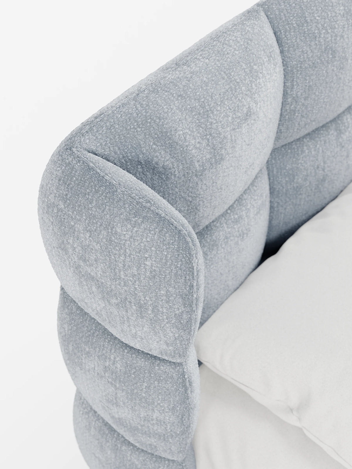 Un primo piano di un letto RAGNAR grigio chiaro, imbottito, con contenitore e testiera capitonné avvolgente, caratterizzato da un design arrotondato con tessuto morbido e testurizzato, parti imbottite e un cuscino bianco a tinta unita appoggiato alla testiera.
