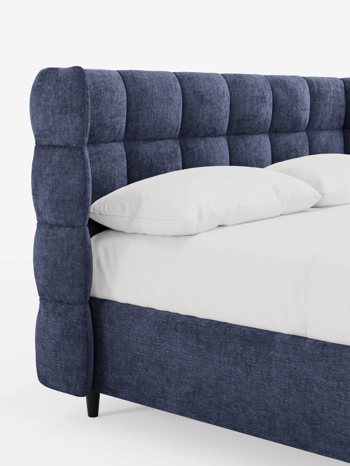 Un primo piano di un letto RAGNAR blu scuro, imbottito, con contenitore e testiera capitonné avvolgente, caratterizzato da una morbida testiera capitonné avvolgente e da lenzuola bianche immacolate sul telaio.