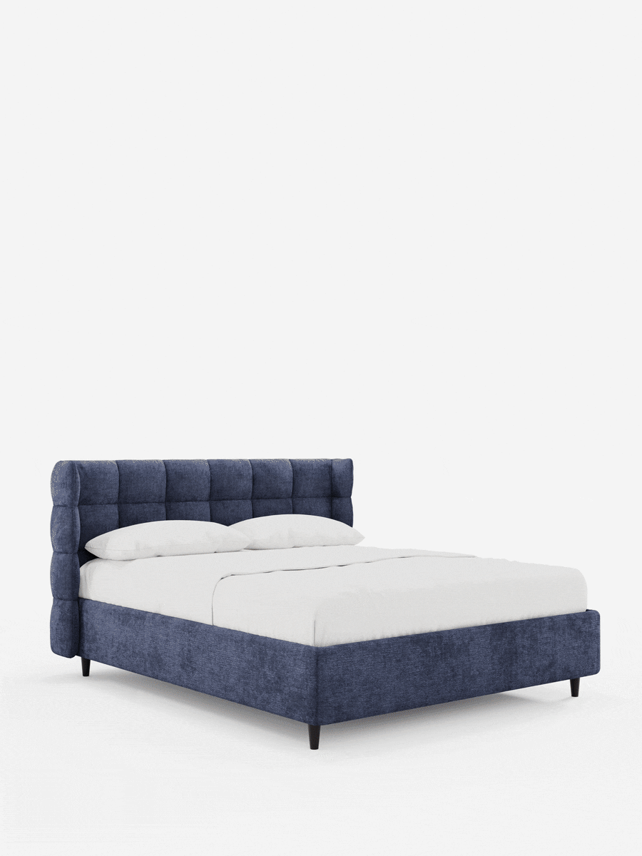 Un letto imbottito RAGNAR blu con contenitore e testiera capitonné avvolgente, con testiera avvolgente e trapuntata a bottoni, si staglia su uno sfondo bianco, rivestito con lenzuola bianche immacolate e sostenuto da quattro gambe scure e affusolate.