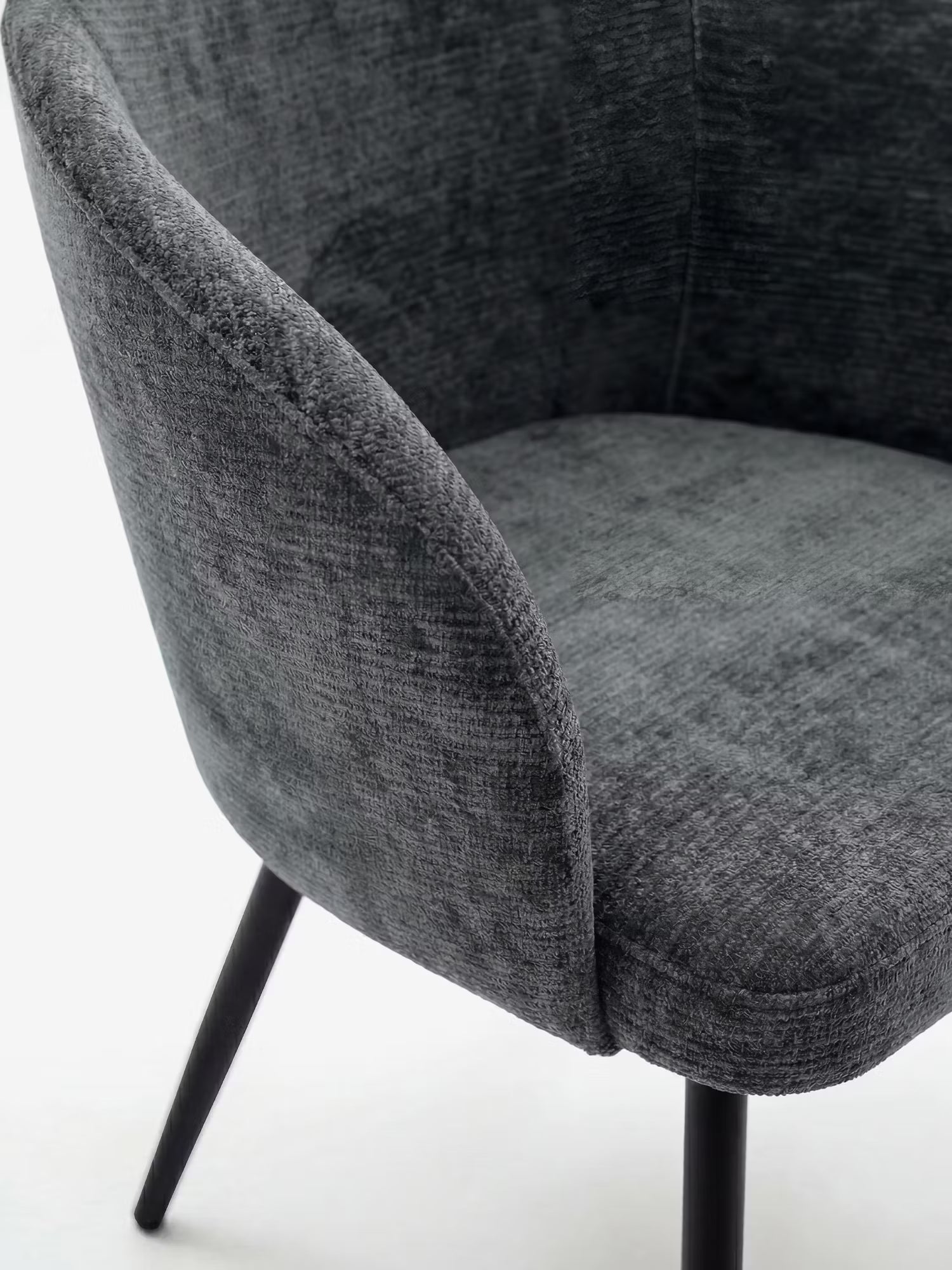Un primo piano della sedia Divani.Store Rovo con braccioli imbottiti e schienale ricurvo in ciniglia, con sottili gambe in metallo nero, ripresa su uno sfondo bianco a tinta unita per mettere in risalto il suo design moderno e il rivestimento grigio scuro dalla trama particolare.