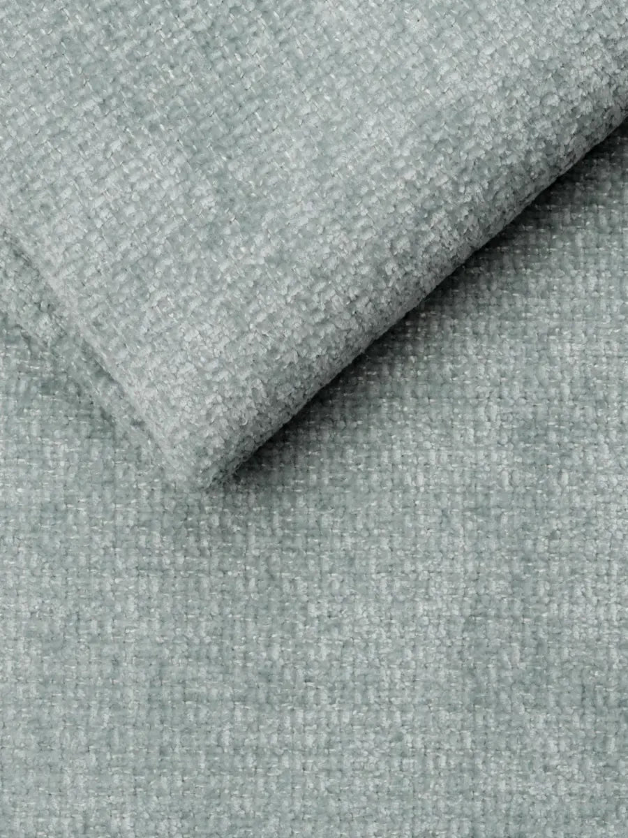 Un primo piano del tessuto azzurro chiaro e materico del divano letto Ottaviano con letto estraibile – penisola reversibile e contenitore in tessuto materico smacchiabile, che mostra un aspetto intrecciato e tattile, piegato in modo da evidenziare la trama fitta e morbida.