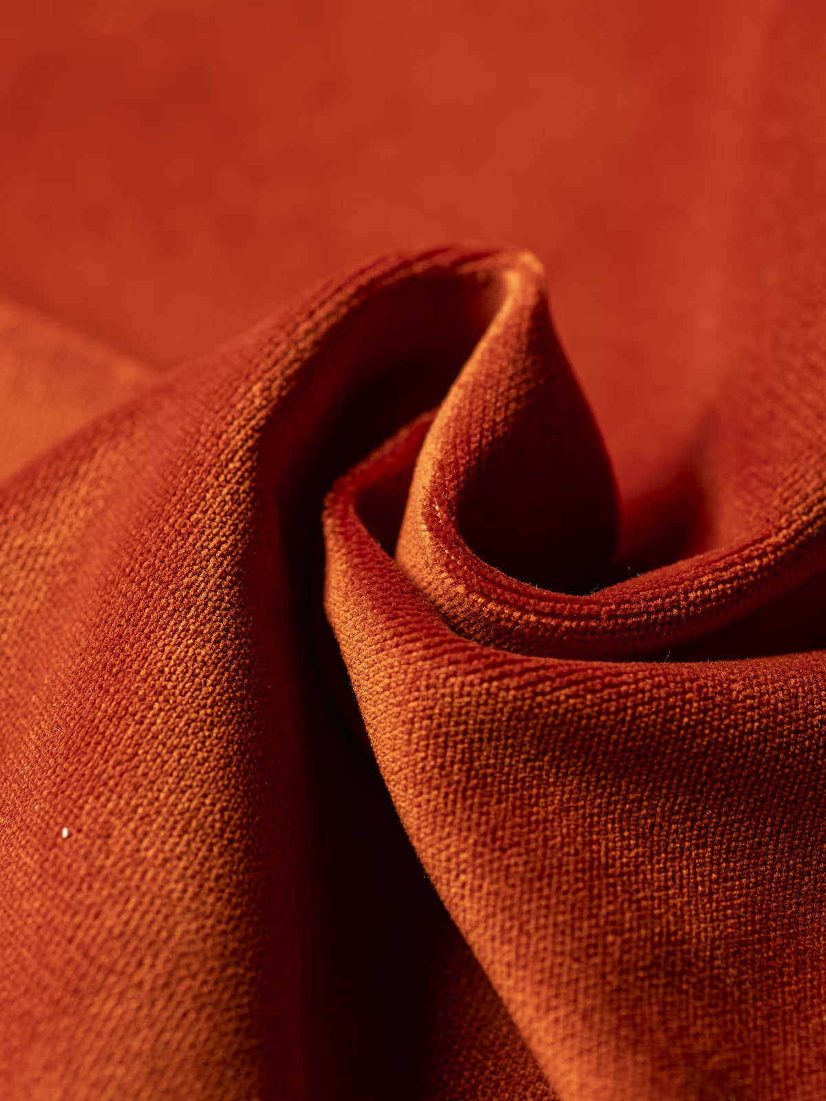 Primo piano del tessuto T30 di Divani.Store, color arancio ruggine e dalla trama rigata, leggermente ritorto per esaltarne l’elegante intreccio e la delicata lucentezza: ideale per il rivestimento del divano letto Francy con poggiatesta regolabili. L’illuminazione mette in risalto la profondità, le ombre e il ricco calore di questo materiale, rimovibile al 100% e resistente alle macchie, creando un’atmosfera accogliente che si adatta perfettamente a qualsiasi disposizione di sedute di stile.