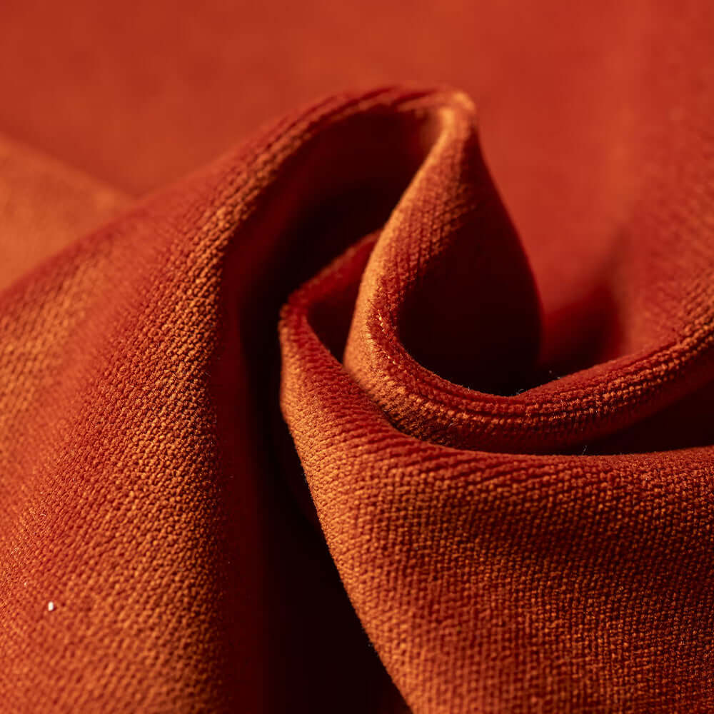Primo piano del T30 Gioiello tessuto Vellutato di Divani.Store: un elegante tessuto arancione-ruggine, morbido al tatto, dalla texture lussuosa e dalla finitura smacchiabile Fast Clean, accuratamente piegato per evidenziarne il calore e il fascino tattile.
