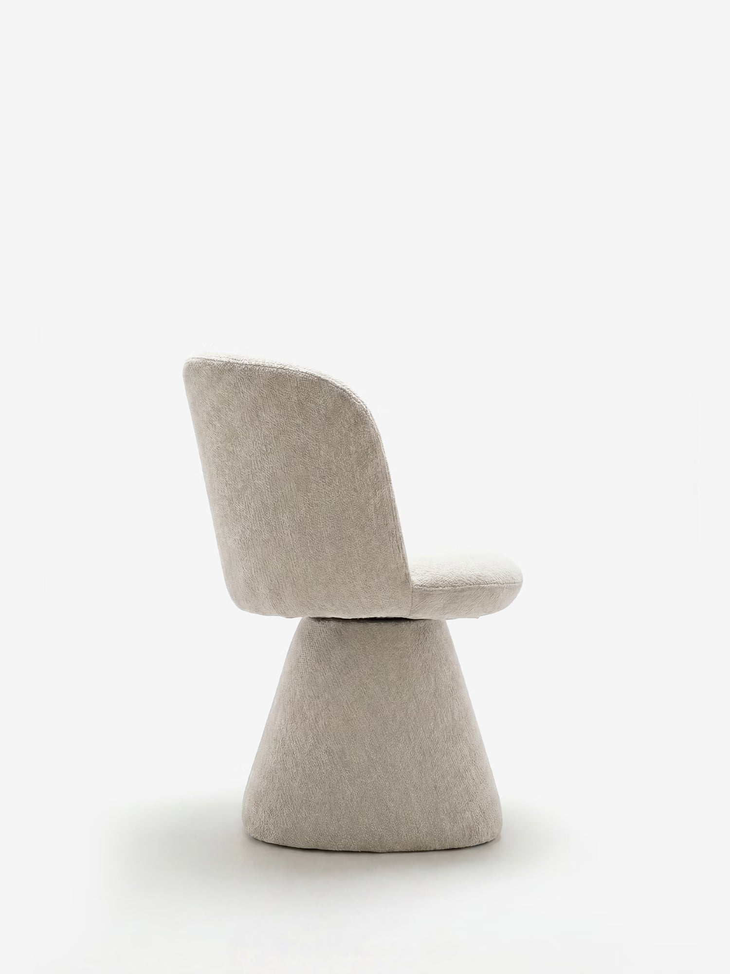 La sedia moderna imbottita Talia di Divani.Store presenta uno schienale e una seduta arrotondati in morbida ciniglia certificata OEKO-TEX®, oltre a un'ampia base imbottita di forma conica. Nella foto è raffigurata di profilo su uno sfondo bianco a tinta unita.