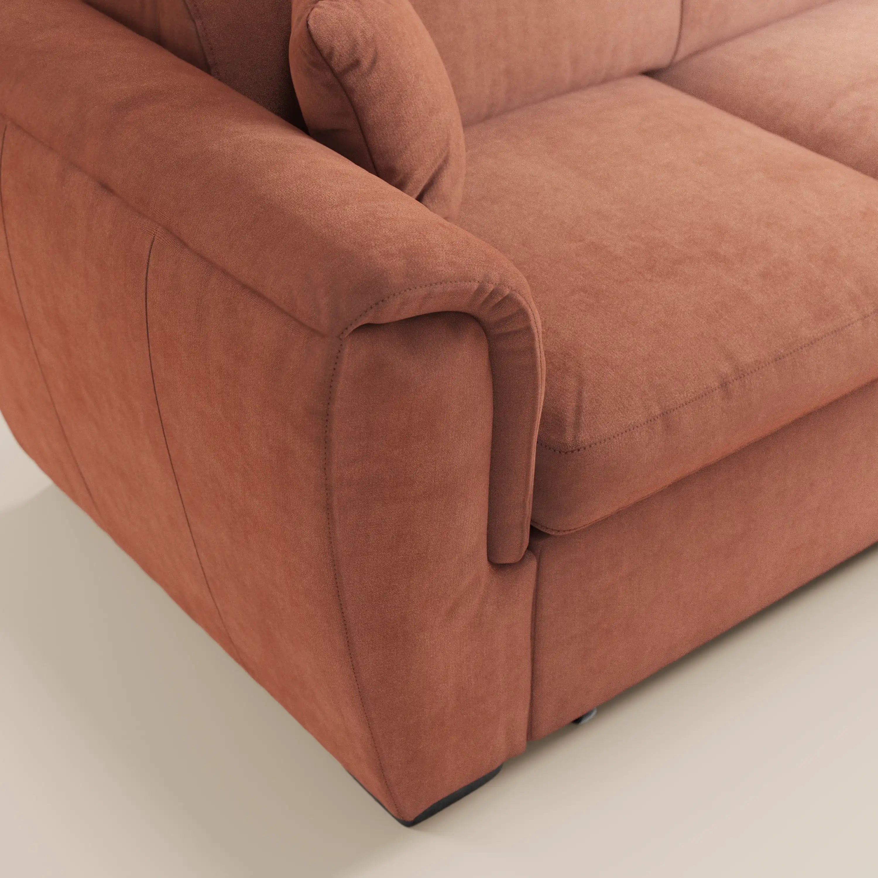 Primo piano del divano angolare reversibile Titano di Divani.Store, realizzato in morbido tessuto Smacchiabile Oeko-Tex® color ruggine, che mette in risalto il bracciolo sinistro imbottito e la seduta. Il divano è dotato di poggiatesta reclinabile e poggia su un pavimento di colore chiaro.