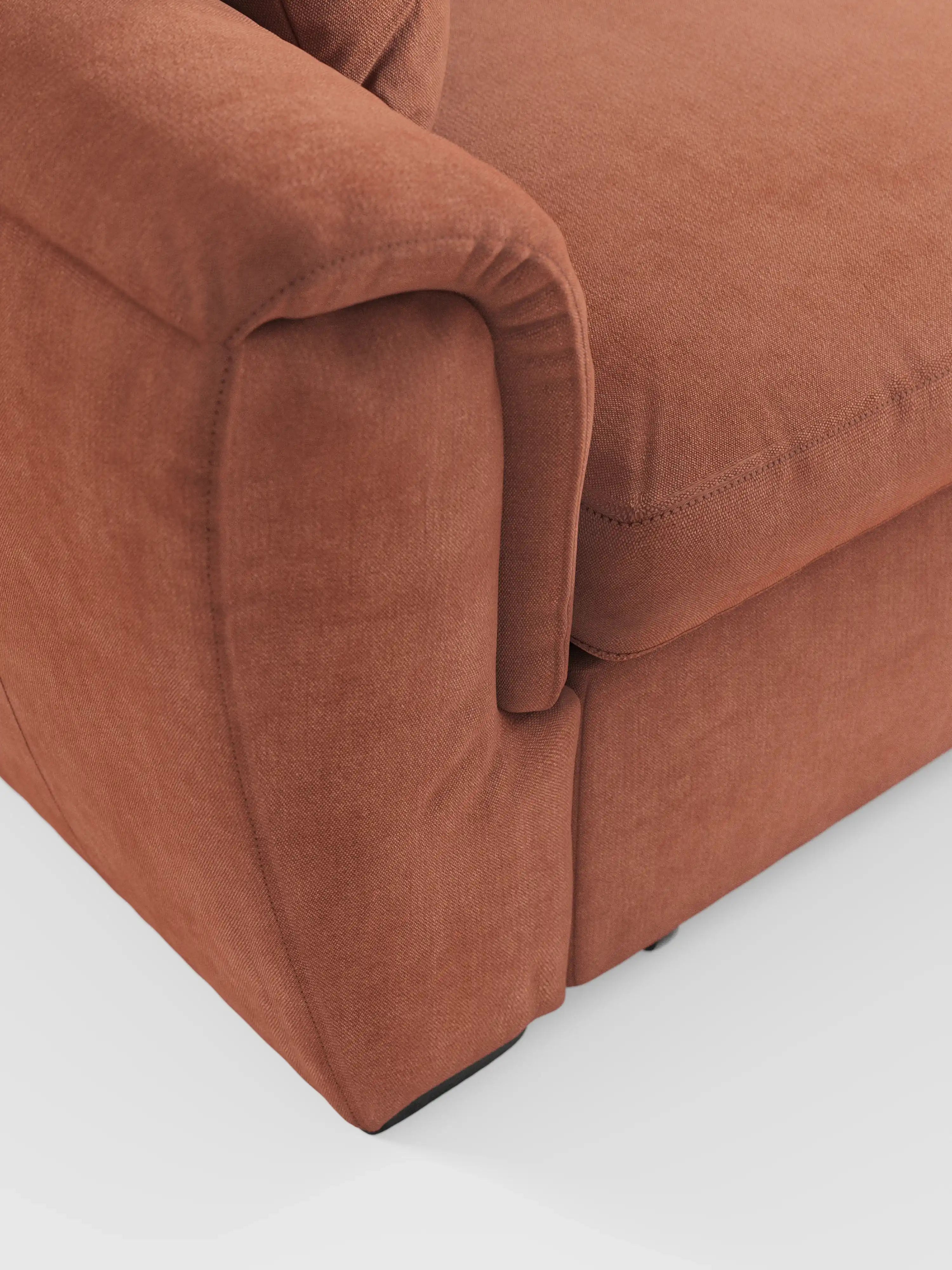 Primo piano del divano angolare reversibile con contenitore estraibile e pouf "Titano" di Divani.Store, rivestito in tessuto color terracotta, resistente alle macchie e certificato Oeko-Tex®. L’immagine mette in risalto il rivestimento morbido e materico dei cuscini dei braccioli e della seduta, con cuciture in evidenza e bordi arrotondati. Uno sfondo bianco a tinta unita esalta il colore caratteristico del divano e i raffinati dettagli del tessuto.
