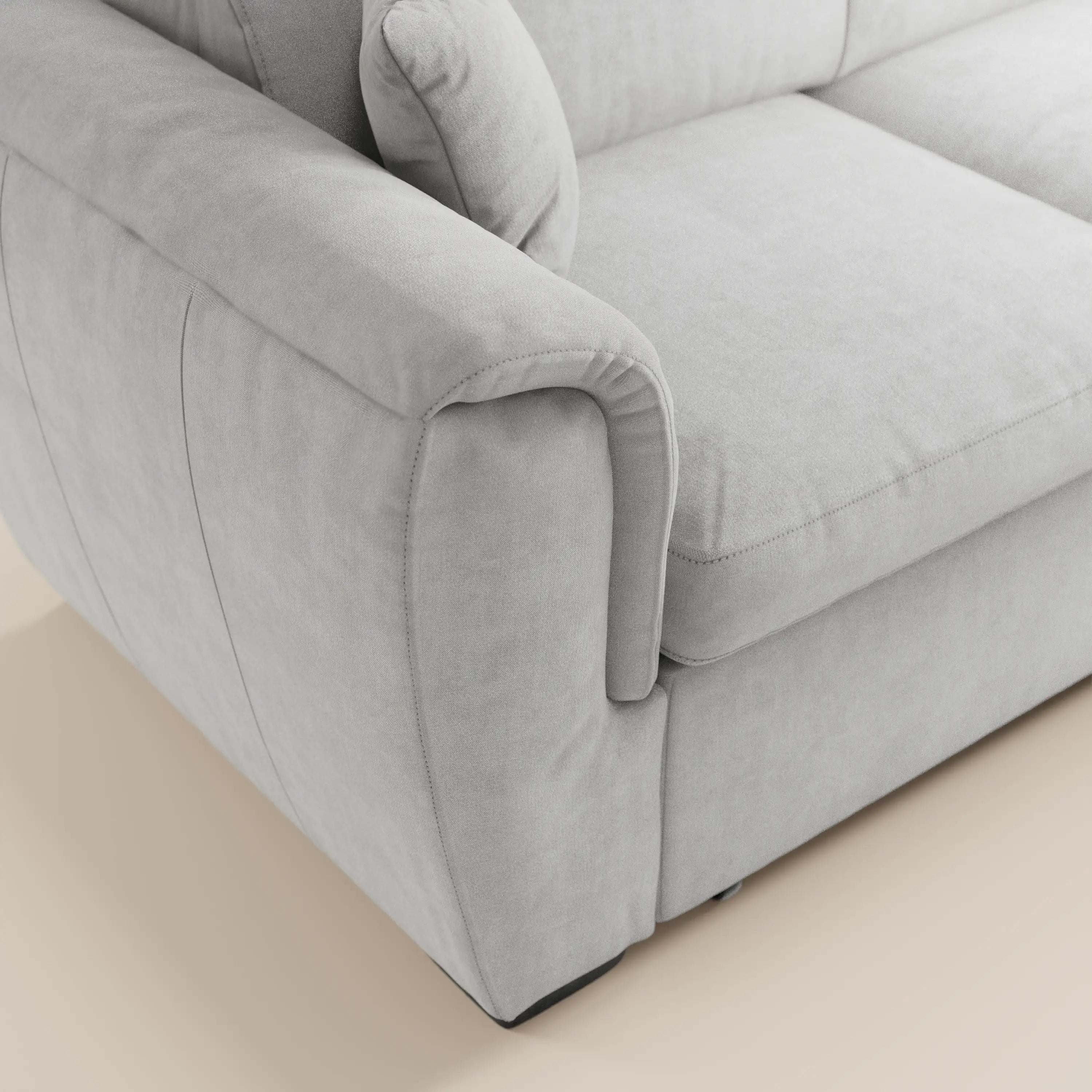 Primo piano del divano angolare reversibile Titano di Divani.Store, realizzato in tessuto grigio chiaro Oeko-Tex® antimacchia, dotato di poggiatesta reclinabili, braccioli spessi, cuscini rigidi, cuscino coordinato e pouf contenitore, su un pavimento beige chiaro.