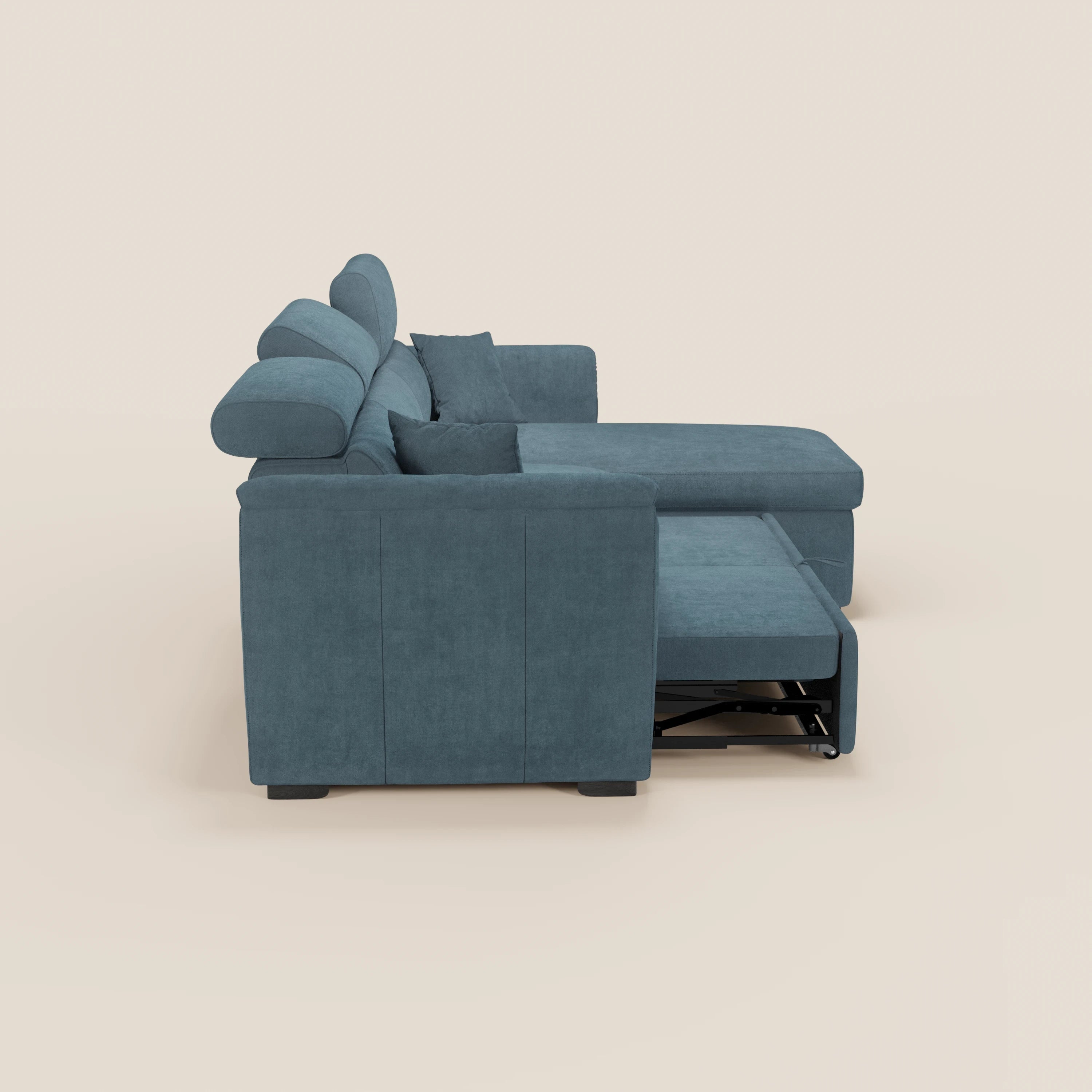 Vista laterale del divano letto Titano con penisola reversibile di Divani.Store in blu, con poggiatesta reclinabili, cuscini morbidi, bracciolo sinistro ed elemento estraibile parzialmente esteso sotto la chaise longue. Sfondo beige chiaro.