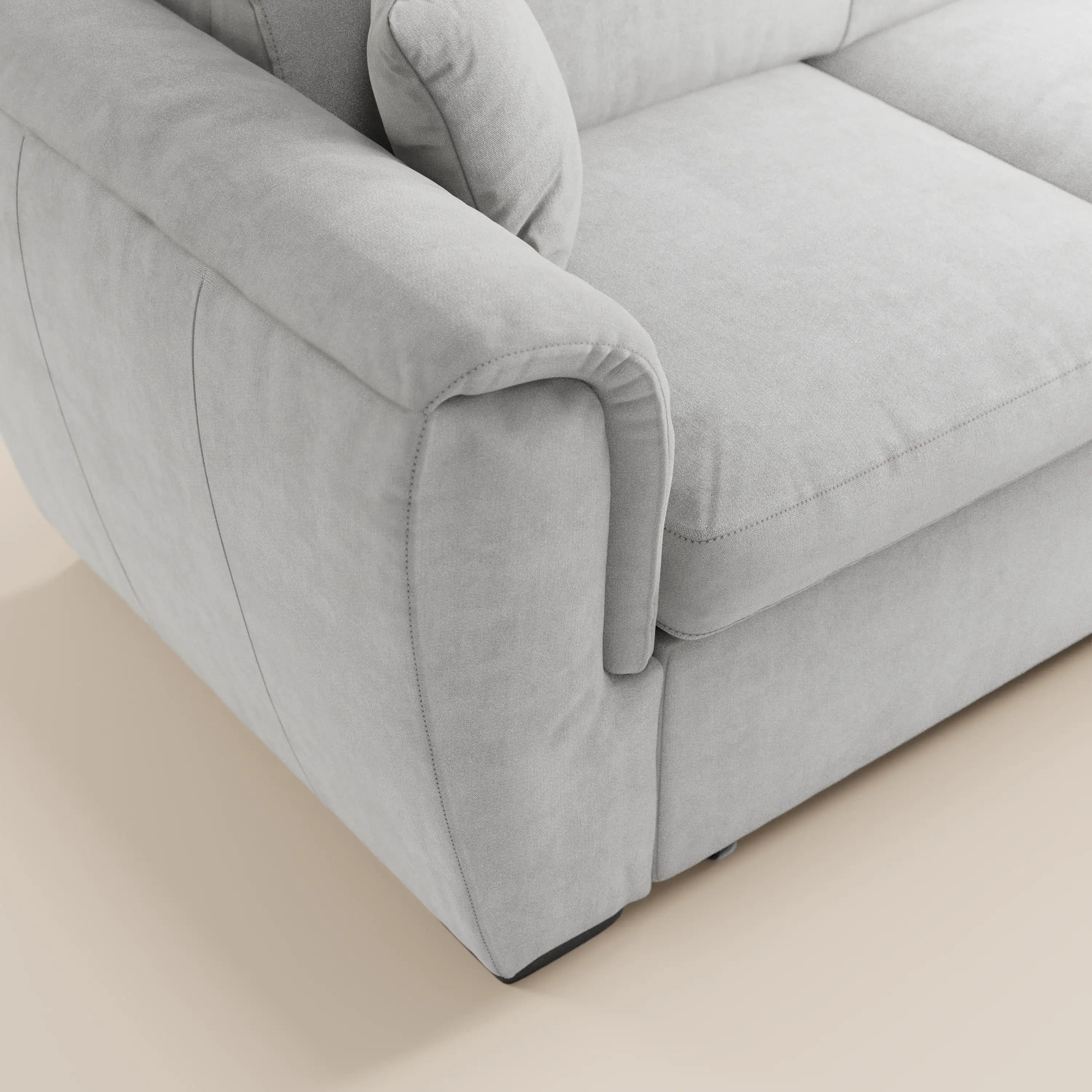 Primo piano del divano letto Titano con penisola reversibile di Divani.Store, dotato di poggiatesta reclinabili, braccioli imbottiti, morbido cuscino di seduta, cuscino coordinato e tessuto antimacchia. Immagine scattata su un pavimento liscio di colore chiaro.