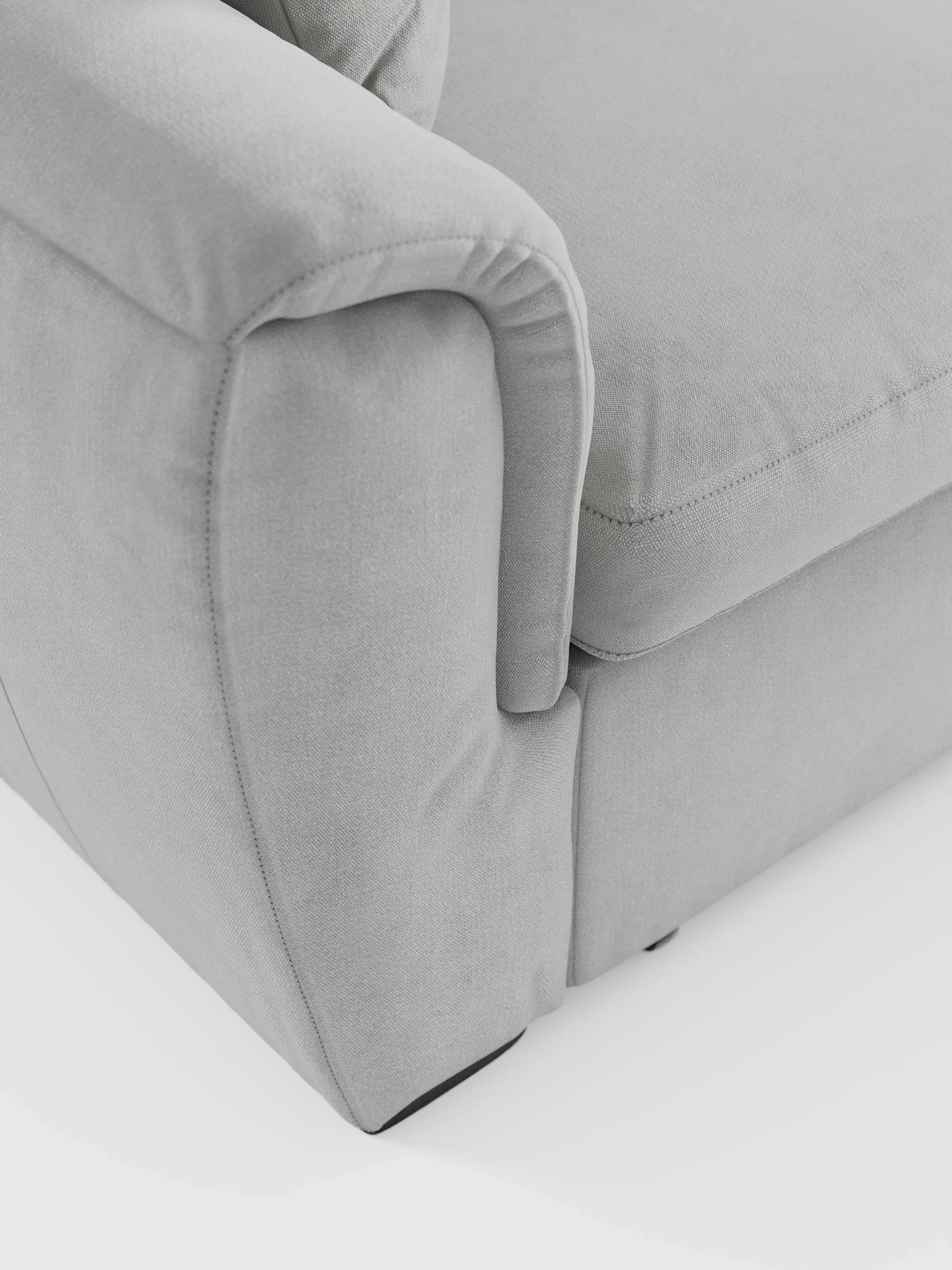 Primo piano di un divano letto Titano con penisola reversibile e contenitore di Divani.Store, rivestito in grigio chiaro, che mette in risalto le cuciture dettagliate, il morbido tessuto antimacchia e l’imbottitura soffice del bracciolo. L'immagine si concentra sull'angolo in cui il bracciolo incontra il cuscino della seduta, mettendo in risalto le linee morbide e pulite e il design contemporaneo tipici di questo divano moderno dotato di poggiatesta regolabili e elemento estraibile.