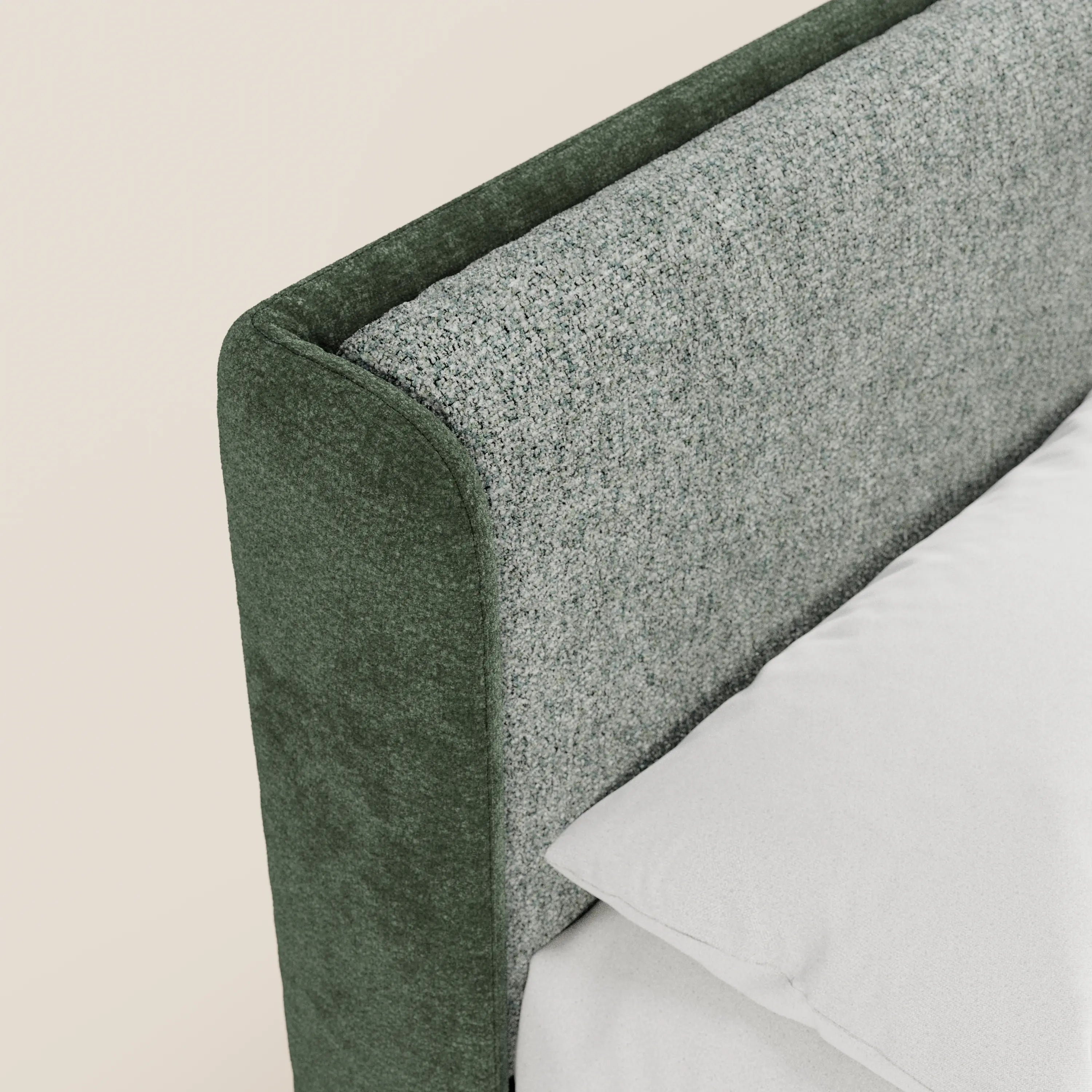 Primo piano del letto imbottito bicolore VALKIRIA di Letti.store, che mostra la testiera curva e avvolgente in grigio chiaro testurizzato con rifiniture in morbido velluto verde scuro. Si intravedono in parte il cuscino bianco e la biancheria da letto; sfondo in una delicata tonalità di beige chiaro.