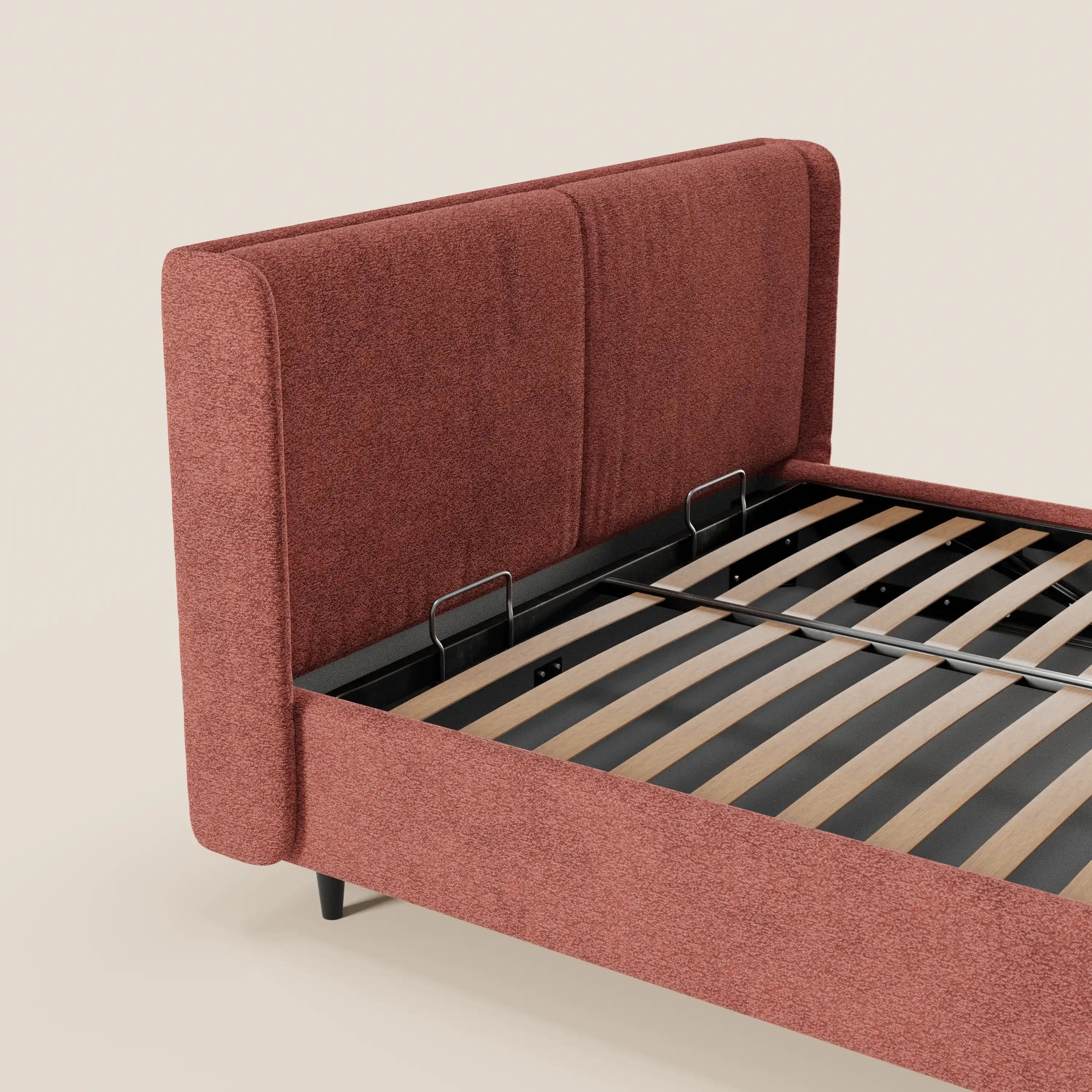 Il letto di design VALKIRIA di Letti.store presenta una testiera rivestita in tessuto rosso-marrone certificato Oeko-Tex® con 2 cuscini imbottiti, pannelli laterali, gambe in metallo nero e doghe in legno per il sostegno, il tutto su uno sfondo beige chiaro.
