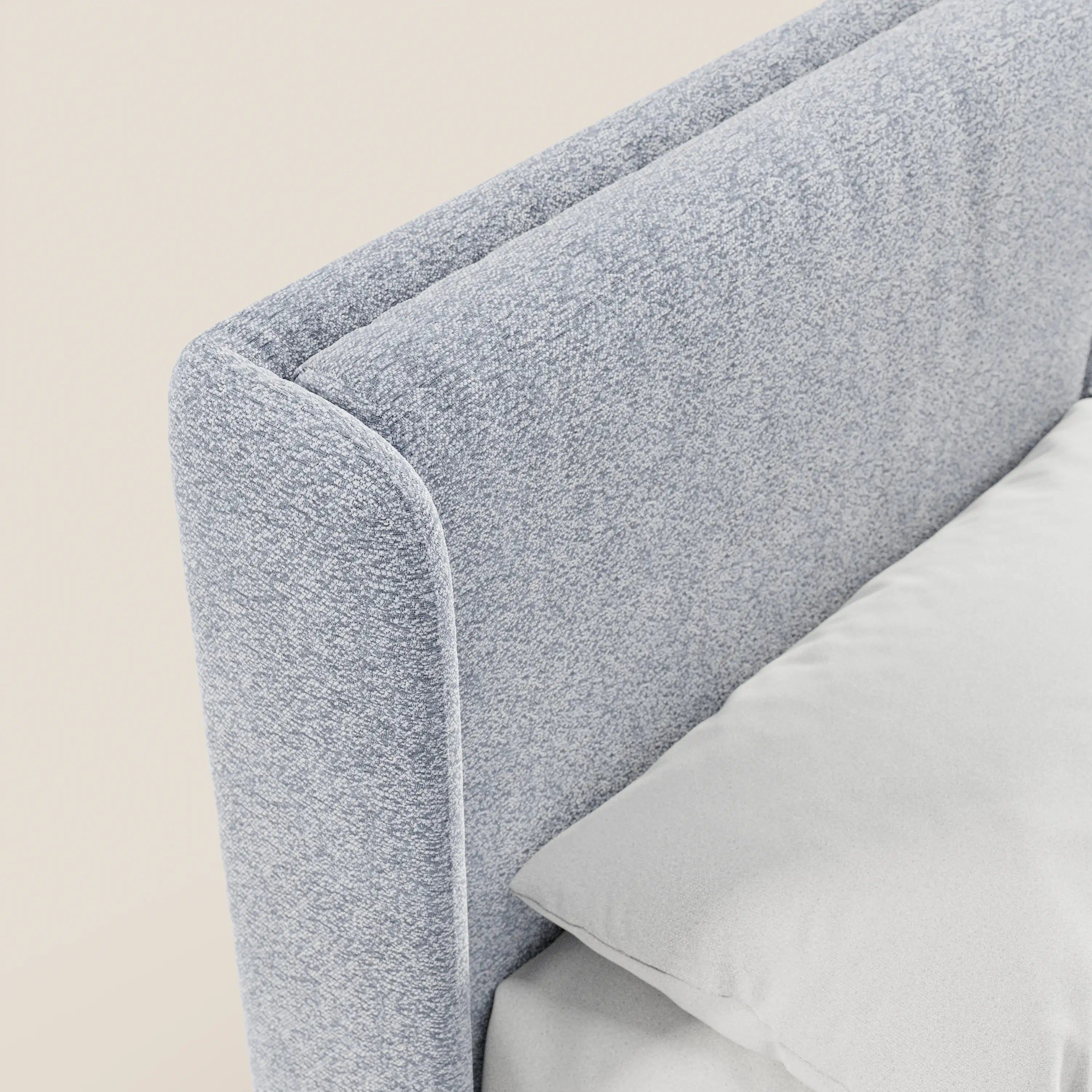 Primo piano di VALKIRIA di Letti.store, un letto di design con contenitore e testiera avvolgente in tessuto Oeko-Tex®. Due cuscini imbottiti, un cuscino bianco e un lenzuolo ne esaltano lo stile contemporaneo e minimalista su uno sfondo beige chiaro.
