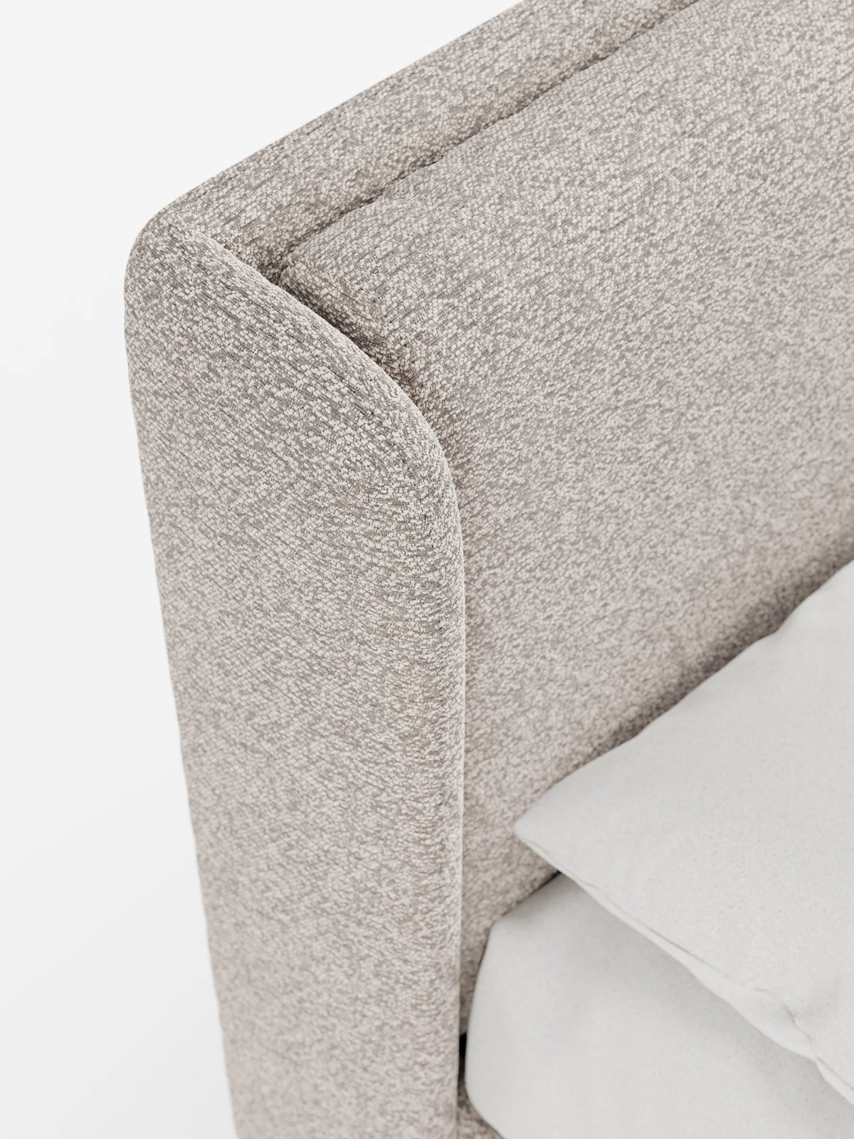 Primo piano di un letto di design VALKIRIA dalla forma curva e avvolgente, con contenitore e testiera avvolgente, rivestito in tessuto grigio chiaro testurizzato, con un cuscino liscio di colore più chiaro posizionato in primo piano.