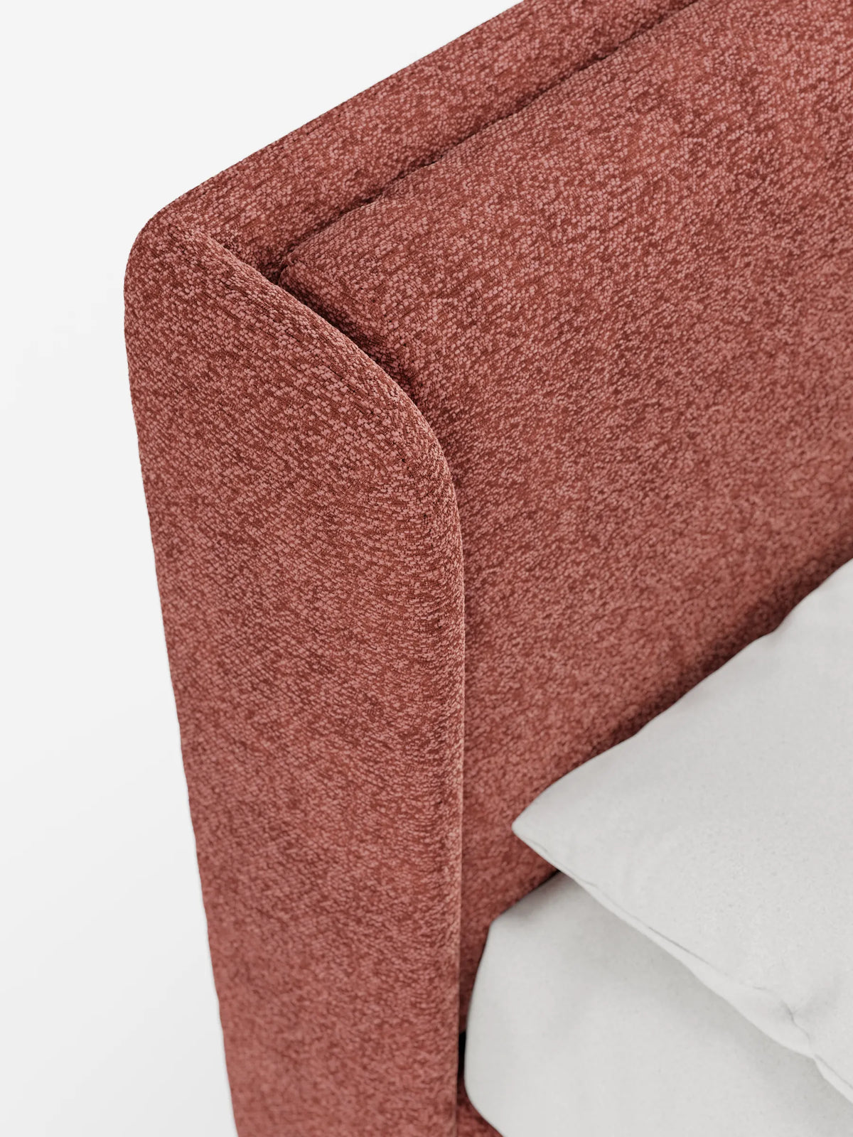 Un primo piano di un letto di design VALKIRIA dalle linee curve e dal colore terracotta, dotato di vano contenitore e testiera avvolgente, caratterizzato da una finitura ruvida e da un cuscino liscio di colore grigio chiaro che fa da contrasto alla struttura su uno sfondo bianco.
