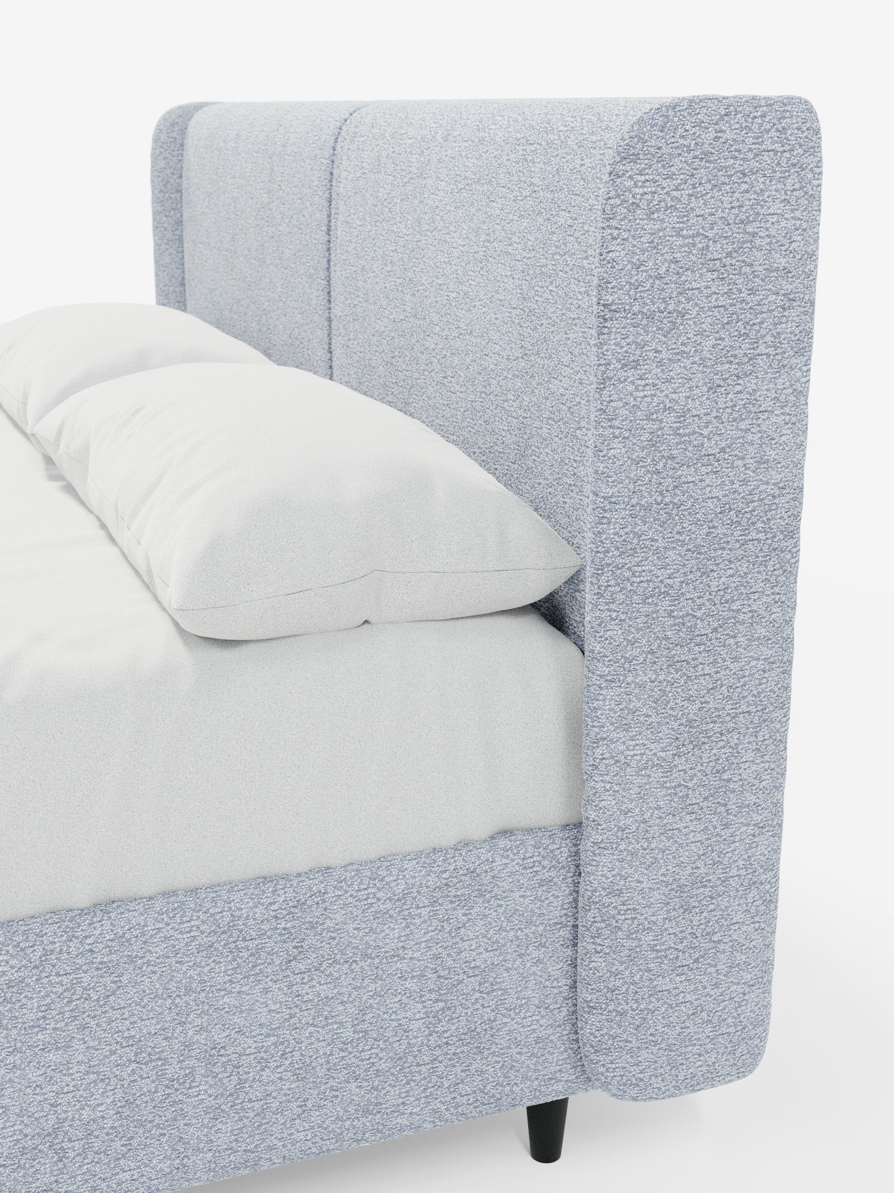 Primo piano del letto di design VALKIRIA con contenitore e testiera avvolgente di Letti.store, rivestito in tessuto grigio chiaro certificato Oeko-Tex®. L’alta testiera imbottita, con due cuscini integrati, ne esalta il design contemporaneo e mette in risalto il tessuto morbido e strutturato dagli angoli arrotondati. Il letto è abbinato a un lenzuolo con angoli e a un cuscino bianchi, mentre alla base si intravedono parzialmente le eleganti gambe nere.