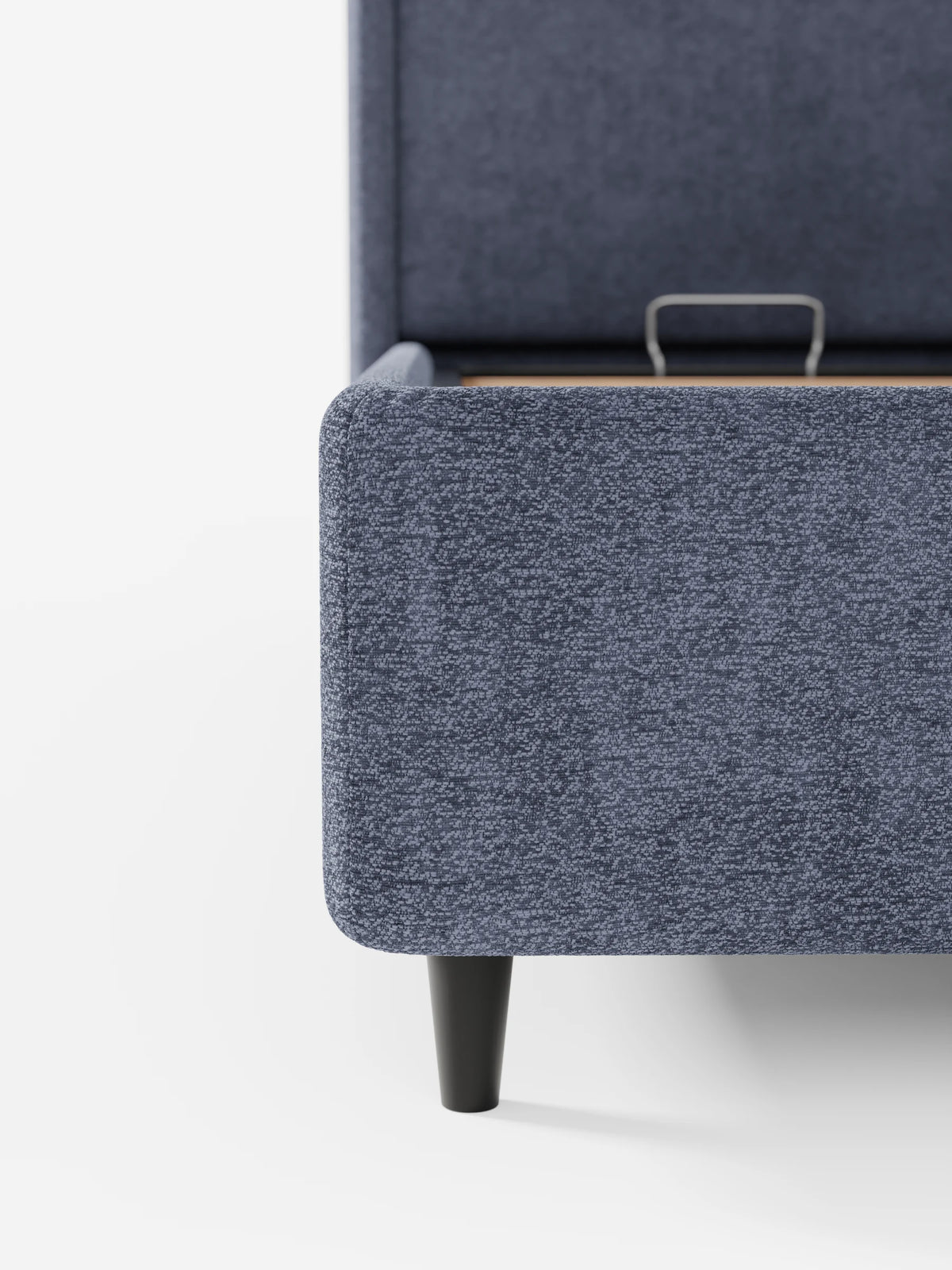 Un primo piano del letto di design VALKIRIA con contenitore e testiera avvolgente - 2 cuscini imbottiti e rivestimento in tessuto Oeko-Tex® blu navy, caratterizzato da una testiera alta e da una gamba in legno scuro affusolata su sfondo bianco.