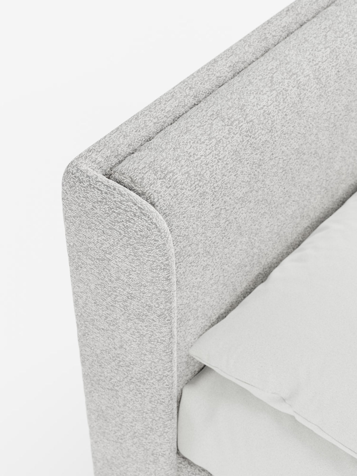 Primo piano di un letto di design VALKIRIA grigio chiaro con vano contenitore e testiera avvolgente di Letti.store, che mette in risalto la morbida trama del tessuto Oeko-Tex® all’angolo della struttura del letto. Il letto in stile contemporaneo comprende due cuscini imbottiti abbinati e un materasso coordinato, tutti realizzati in tessuto grigio chiaro simile, che risaltano sullo sfondo bianco a tinta unita. La prospettiva dall’alto mette in risalto la cura dei dettagli nella lavorazione degli angoli.