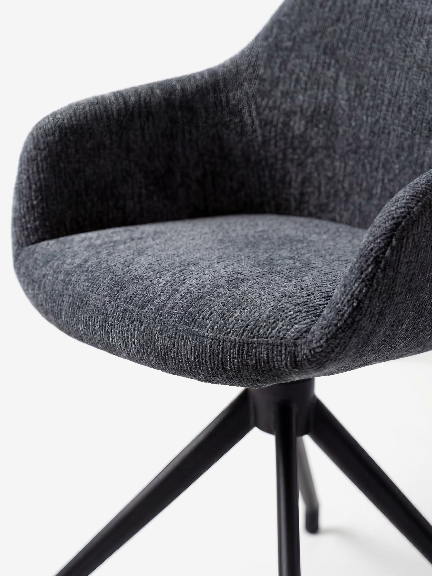 Un primo piano della sedia imbottita Vico di Divani.Store, realizzata in tessuto OEKO-TEX® morbido al tatto di colore grigio scuro, con braccioli ricurvi, seduta imbottita e robuste gambe in metallo nero. Lo sfondo bianco minimalista ne esalta il design contemporaneo.