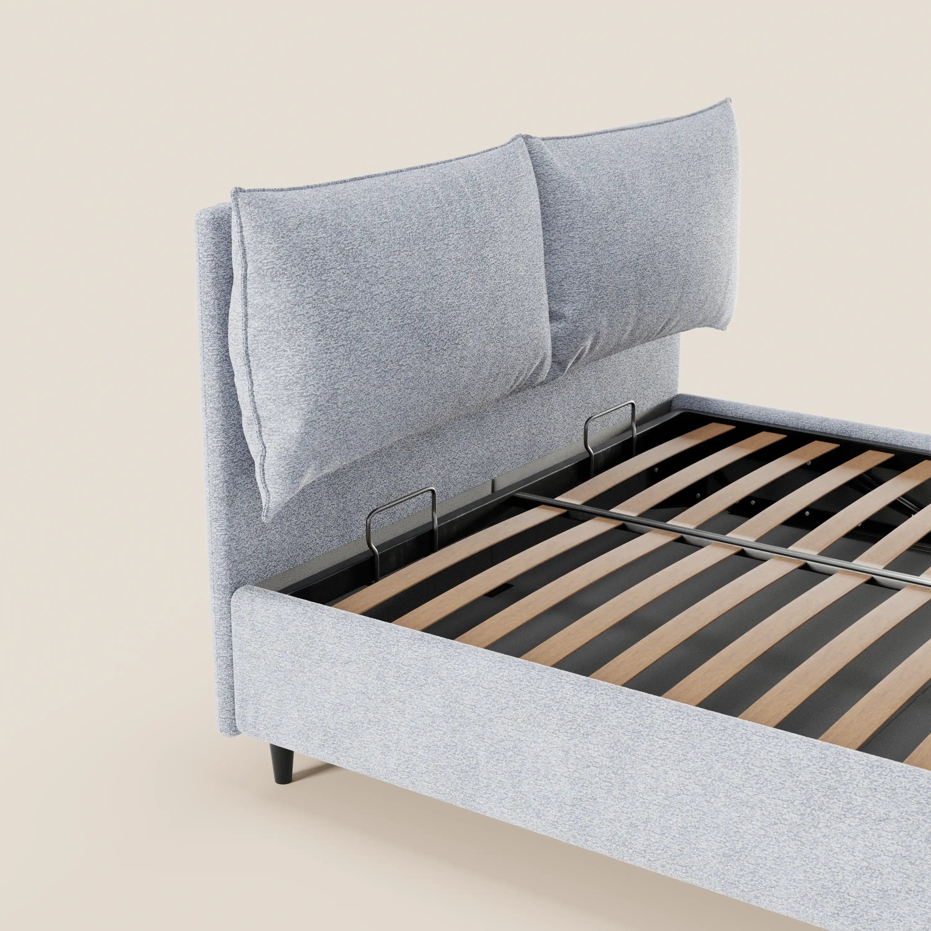 Il letto imbottito ZAYRON di Letti.store è raffigurato in primo piano con una testiera in tessuto grigio chiaro certificato Oeko-Tex®, due grandi cuscini regolabili, doghe in legno e una base contenitore. Design moderno e minimalista su uno sfondo beige a tinta unita; materasso e biancheria da letto non inclusi.