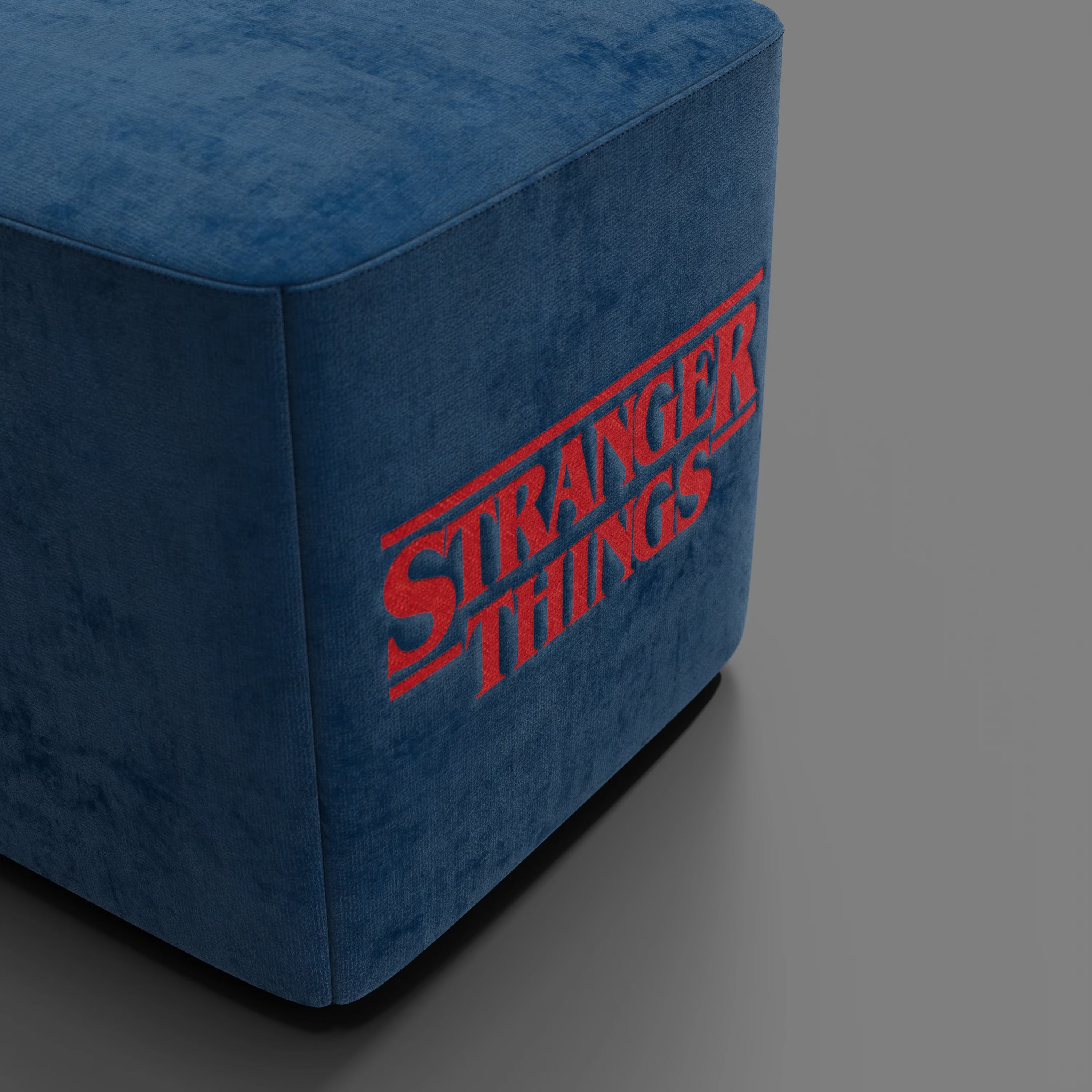 Il pouf Cube Stranger Things Edition di Divani.Store, in tessuto blu antimacchia con l'iconico logo, dona un tocco di cultura pop a qualsiasi spazio su un semplice sfondo grigio.