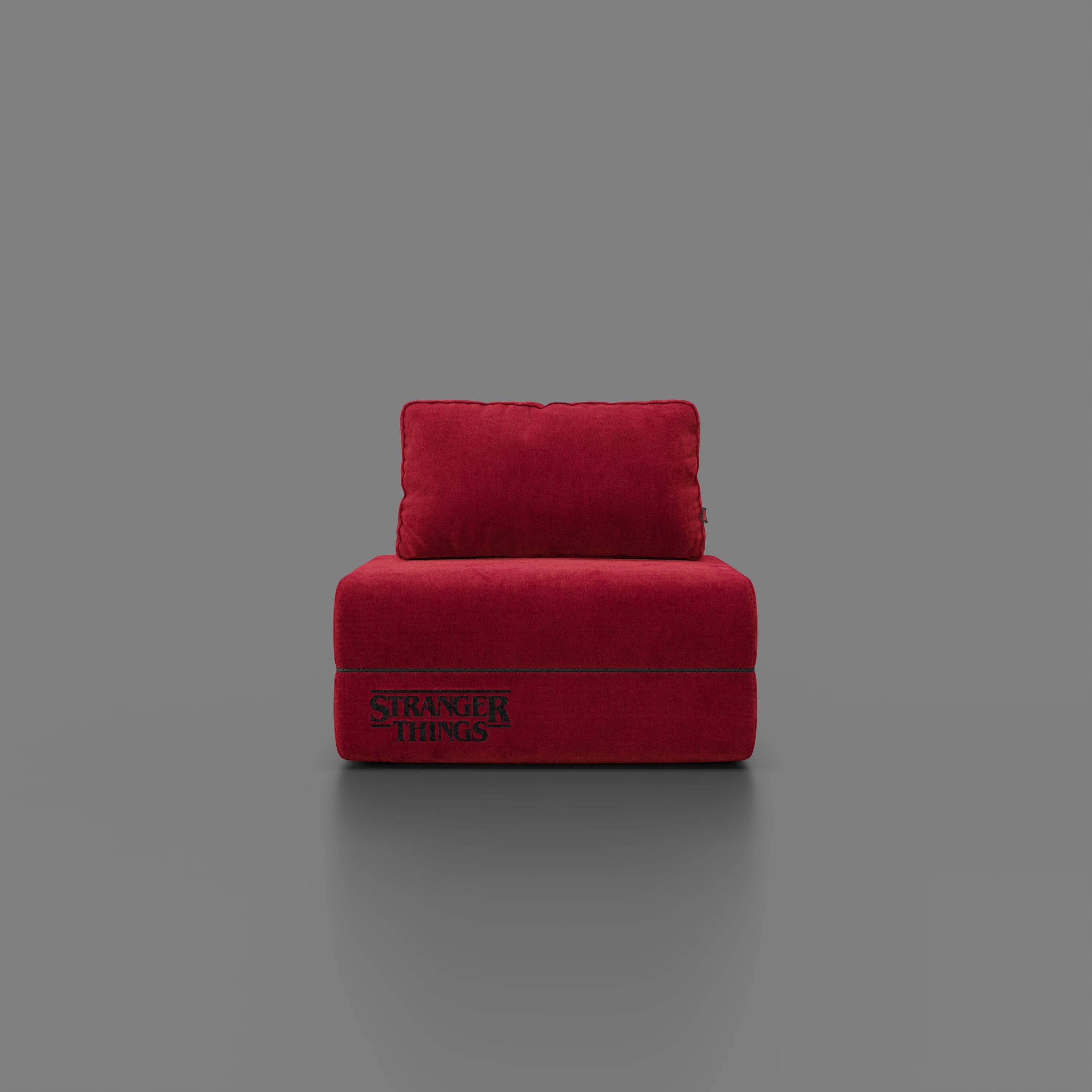 Centrata su uno sfondo grigio, la poltrona letto Rift STRANGER THINGS Edition di Divani.Store è caratterizzata da un tessuto rosso antimacchia, da un materasso in memory foam alto 22 cm e da un cuscino con il logo di "Stranger Things", ideale per qualsiasi configurazione Netflix.