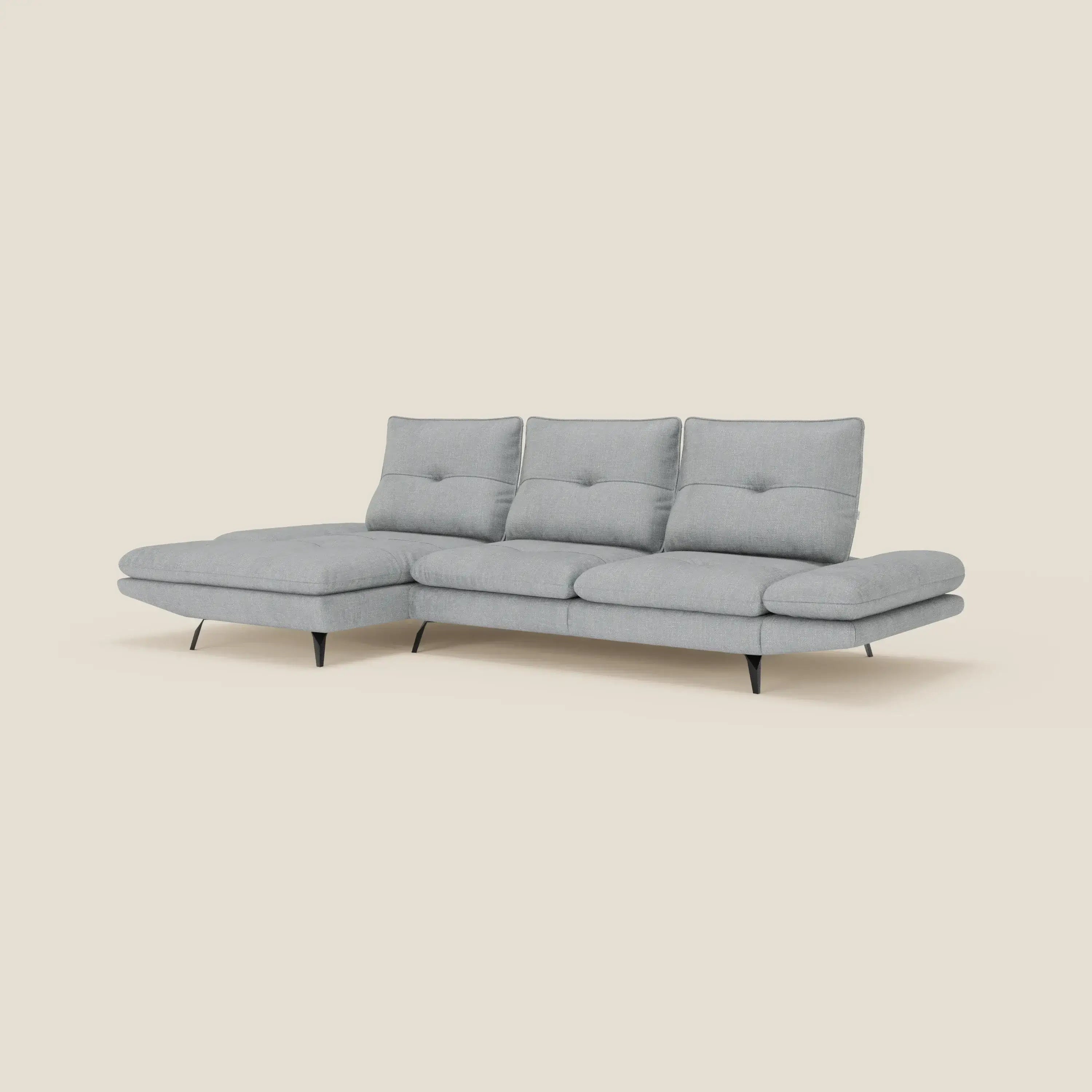 Ardex Divano con penisola di Divani.Store è caratterizzato da schienali scorrevoli, braccioli regolabili ed elegante tessuto impermeabile T06 ghiaccio, con un design moderno e minimalista e sottili gambe nere, su uno sfondo bianco sporco.