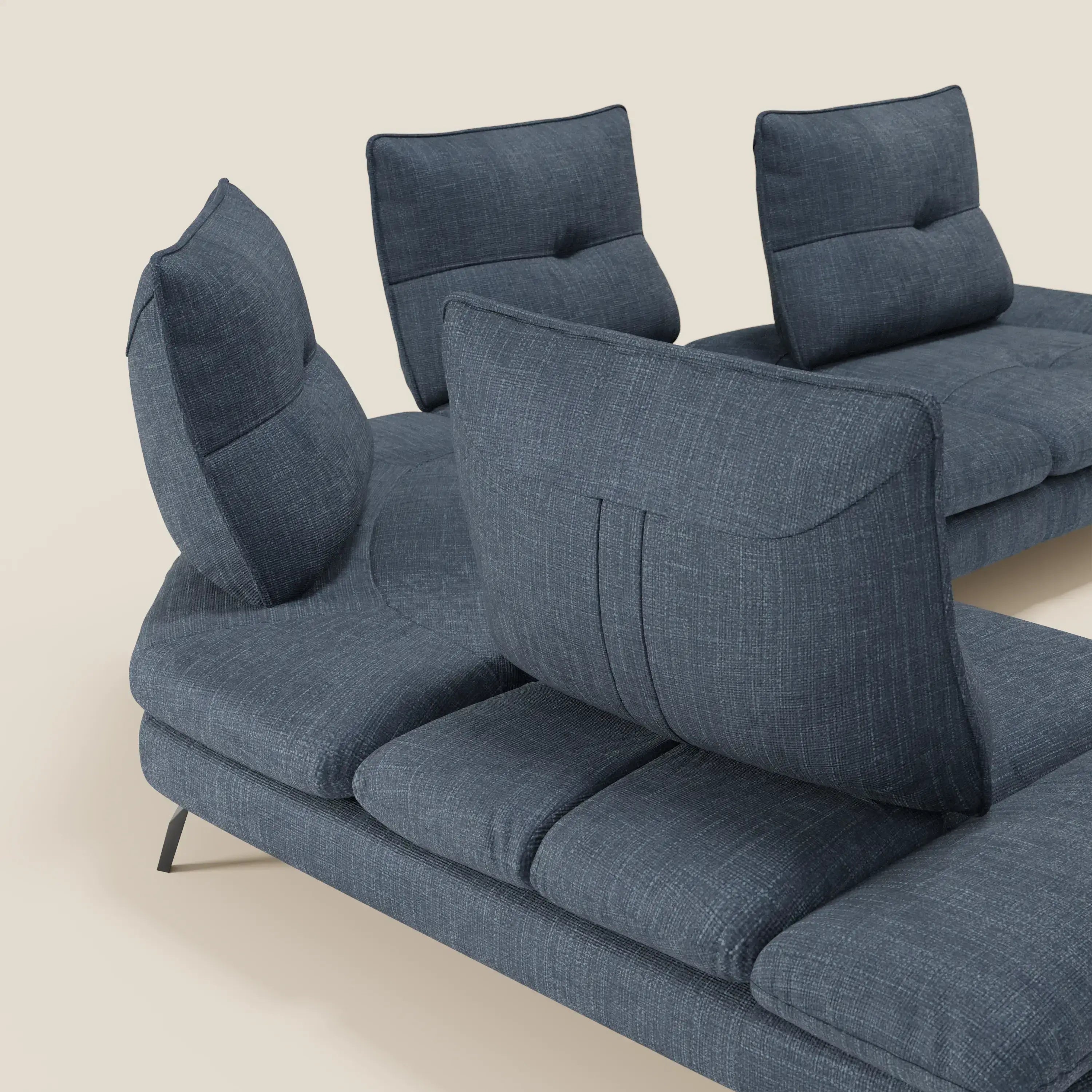 L'Ardex Divano Angolare di Divani.Store in tessuto impermeabile blu T06 è caratterizzato da schienali regolabili e scorrevoli e da un bracciolo mobile, con cuciture a vista e gambe in metallo nero, su sfondo beige.