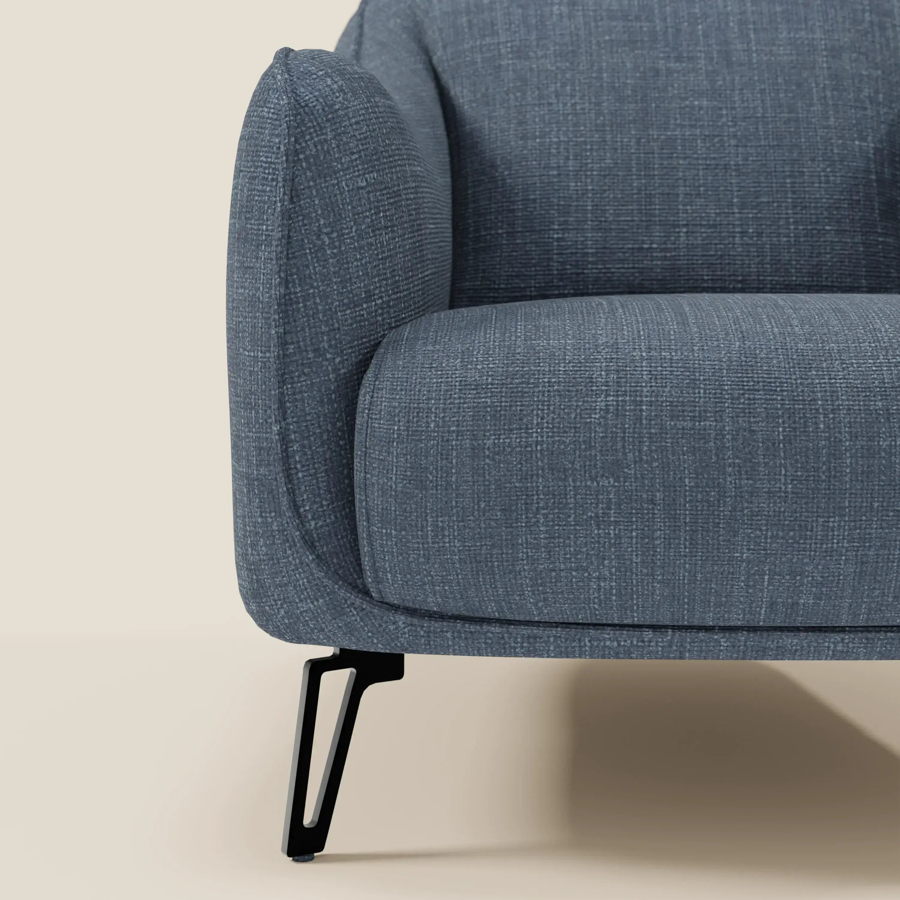 Primo piano di Avela Poltroncina di Divani.Store, con bracciolo sinistro e seduta in morbido tessuto T06 blu impermeabile, dal design moderno ed elegante su sottili gambe in metallo nero su sfondo beige.