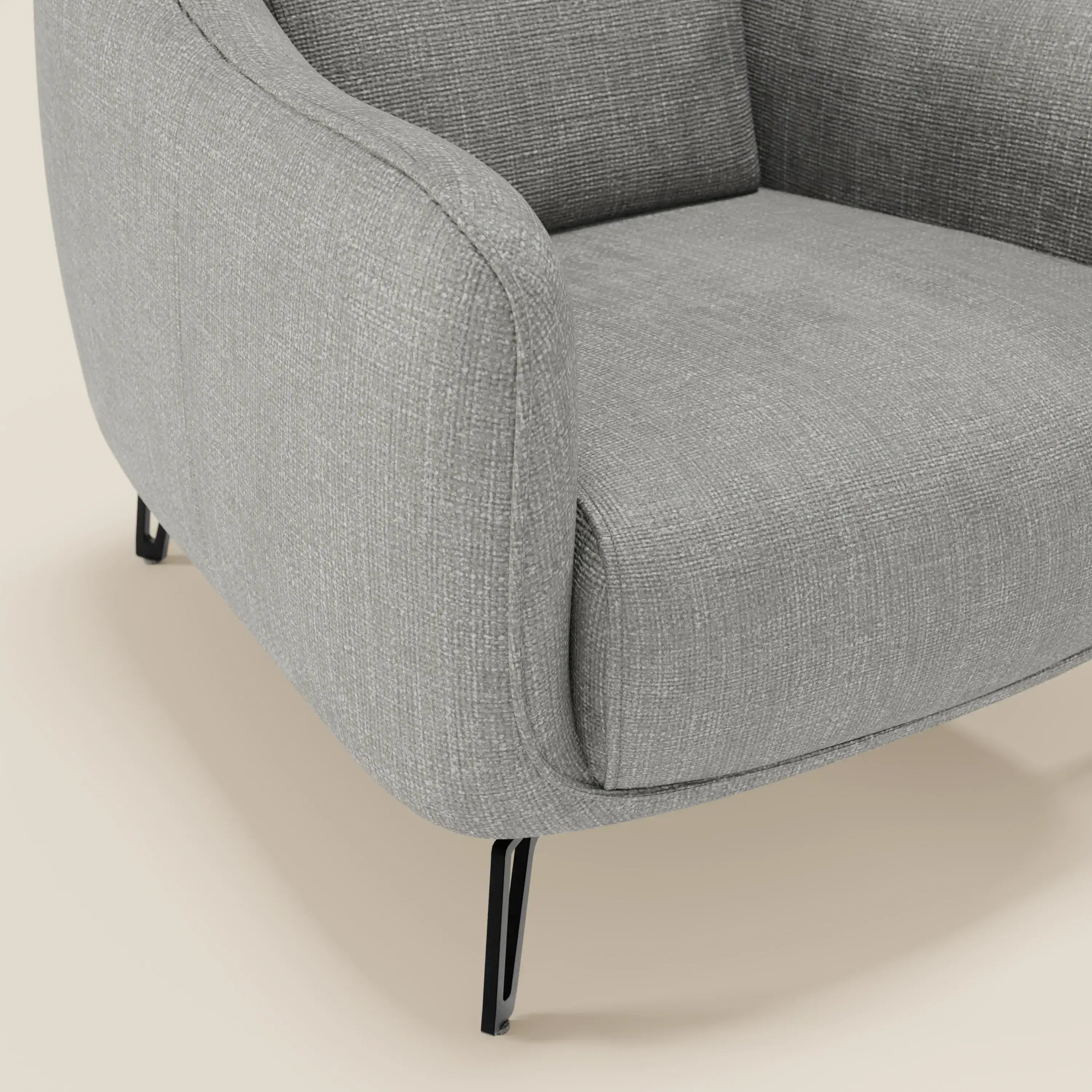 Primo piano di Avela Poltroncina di Divani.Store, caratterizzata da un comfort senza tempo e da un morbido tessuto impermeabile grigio T06, con braccioli curvi e gambe sottili e angolate in metallo nero su uno sfondo liscio color crema chiaro.